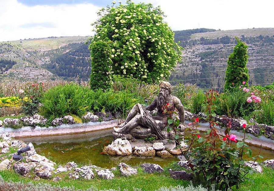 a statue of a man sitting on a rock next to a pond in a garden .