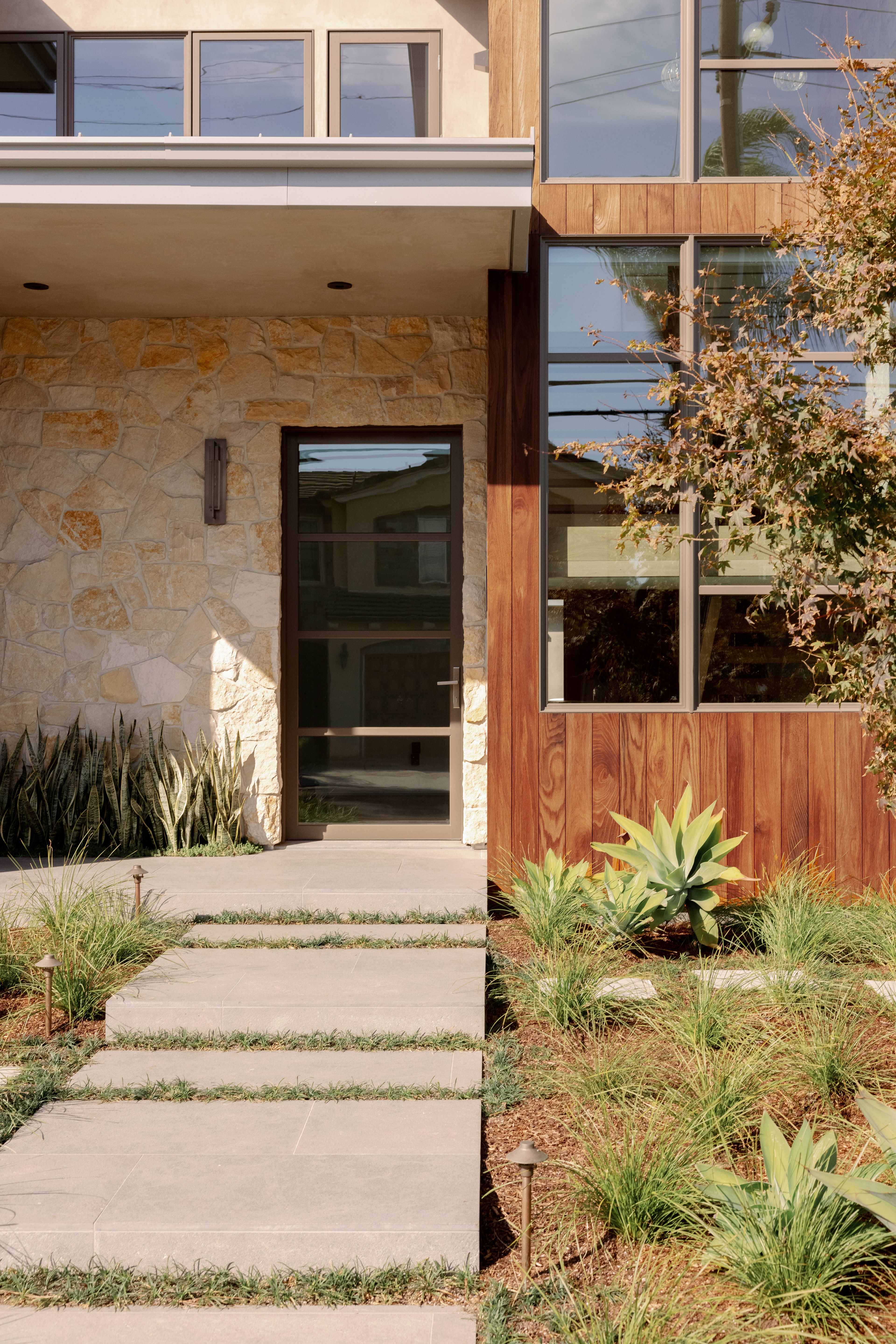 Limestone steps lead to a facade of stone, wood, and smooth trowel stucco