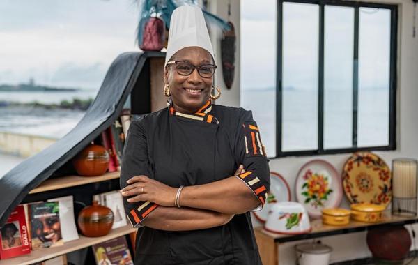 La Cheffe Yaya Barry en tenue professionnelle, dressant un plat gastronomique fusion mettant en valeur les produits du terroir guinéen.