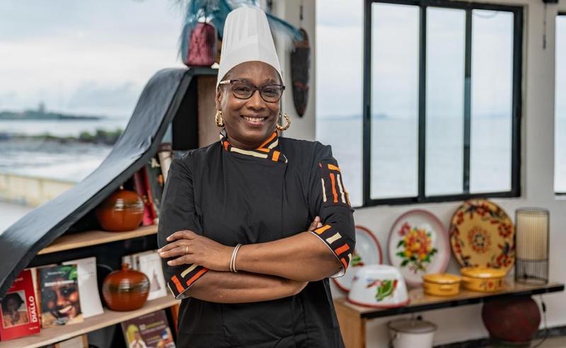 La Cheffe Yaya Barry en tenue professionnelle, dressant un plat gastronomique fusion mettant en valeur les produits du terroir guinéen.