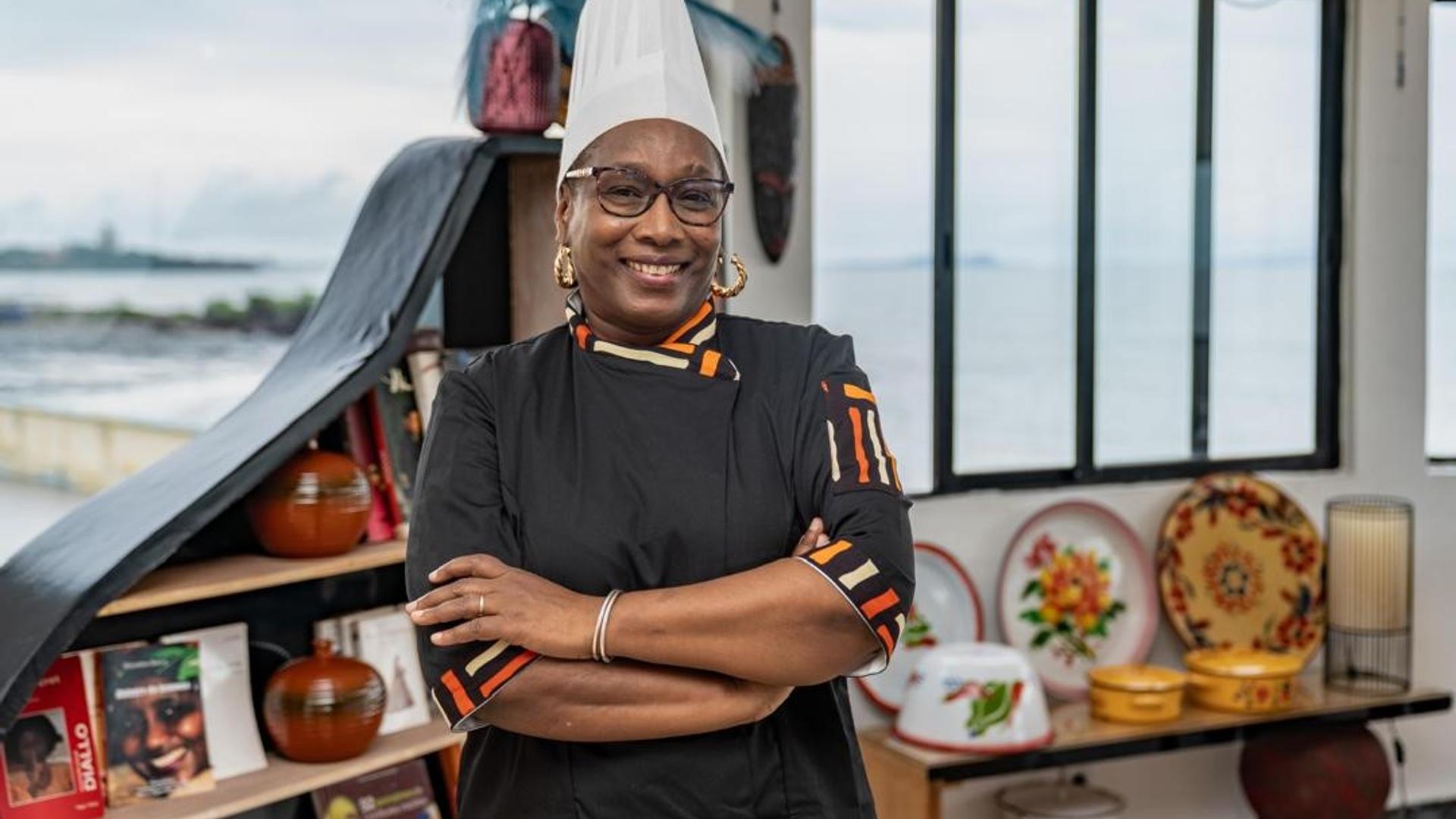 La Cheffe Yaya Barry en tenue professionnelle, dressant un plat gastronomique fusion mettant en valeur les produits du terroir guinéen.