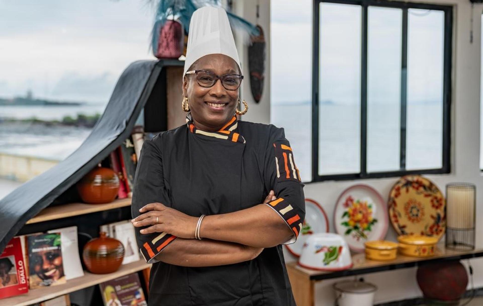 La Cheffe Yaya Barry en tenue professionnelle, dressant un plat gastronomique fusion mettant en valeur les produits du terroir guinéen.