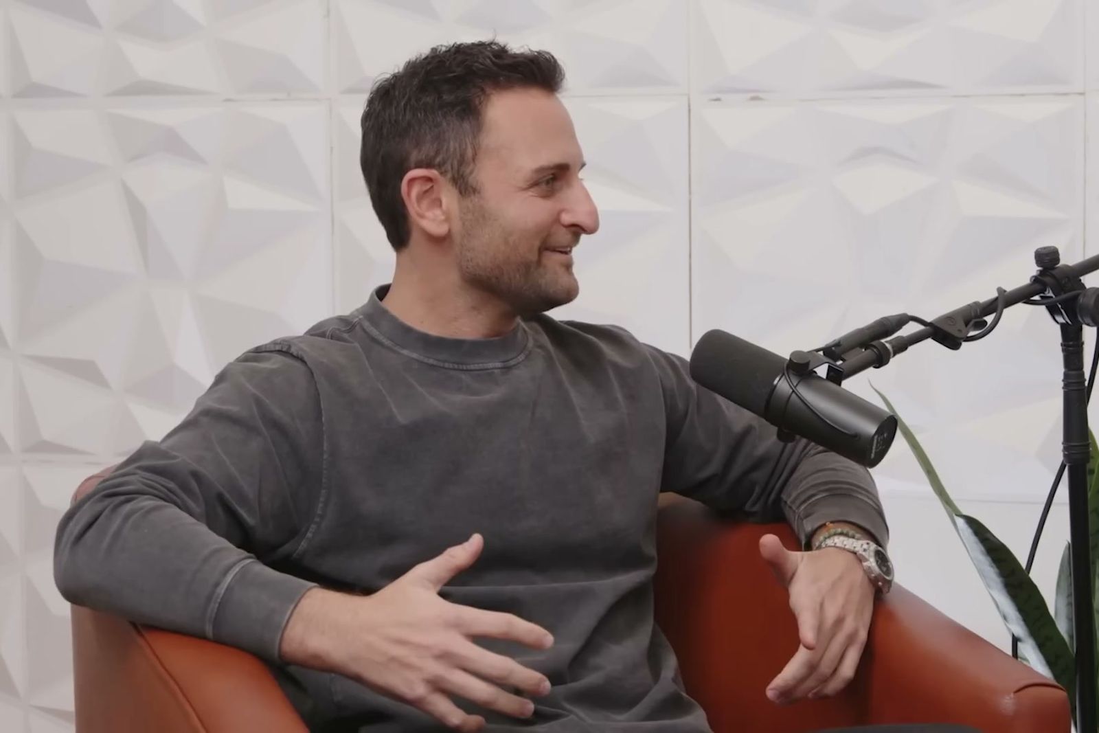 Arthur Leopold laughing in an armchair at a podcast microphone