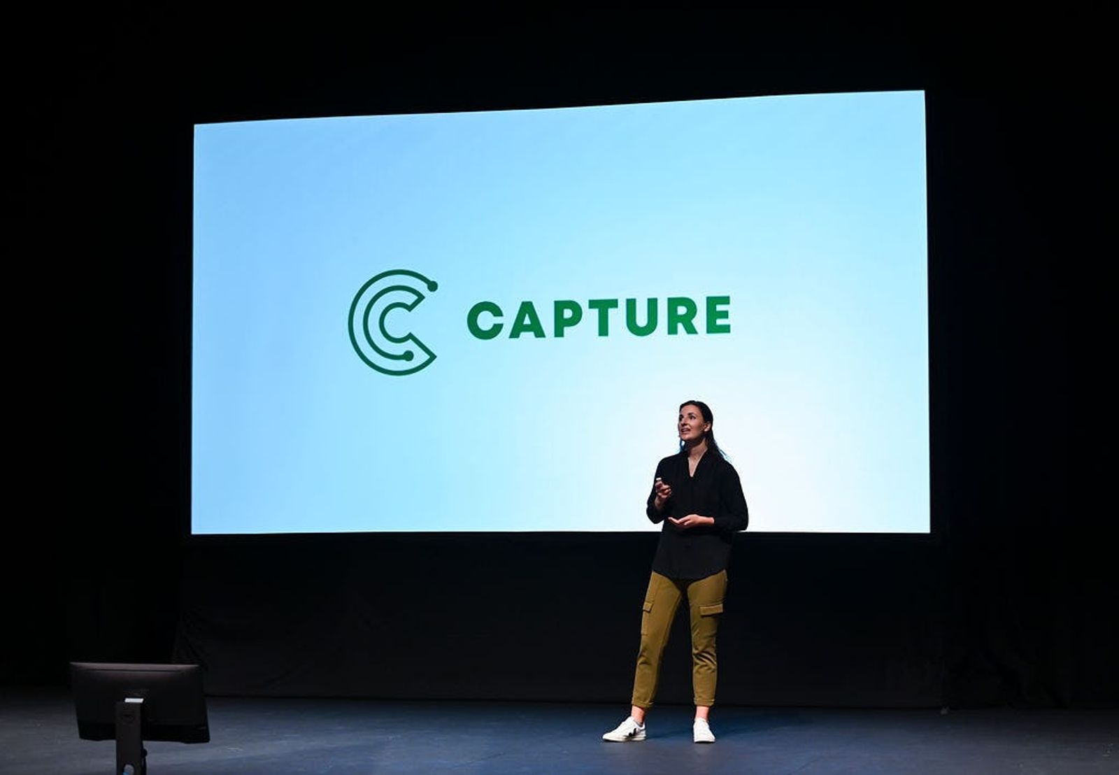 Co-Founder of Capture Josie Stocker does presentation on stage with Capture logo on screen behind her t