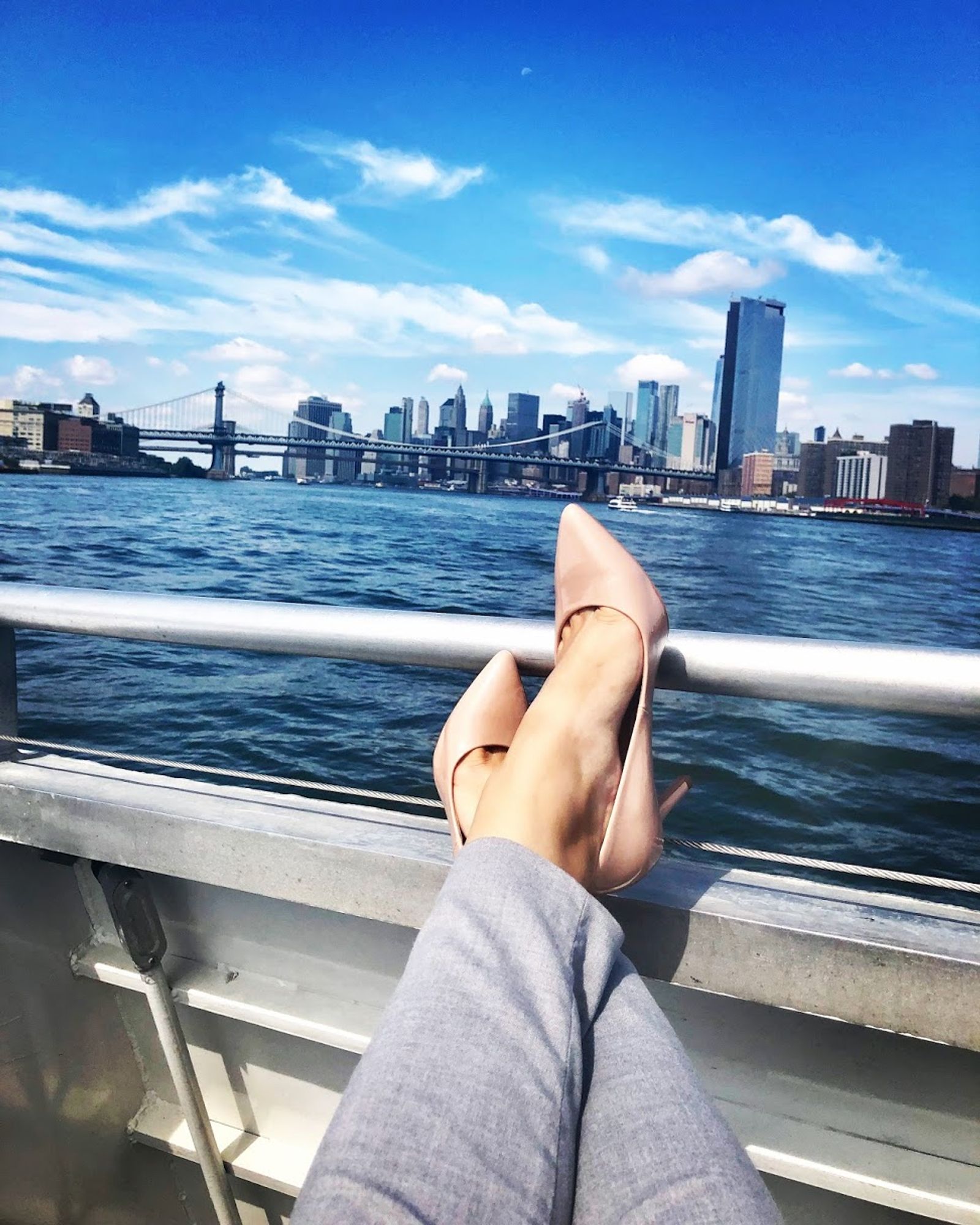 Lady with grey pants and pink high heels putting feet up on boat with city skyline in the background 