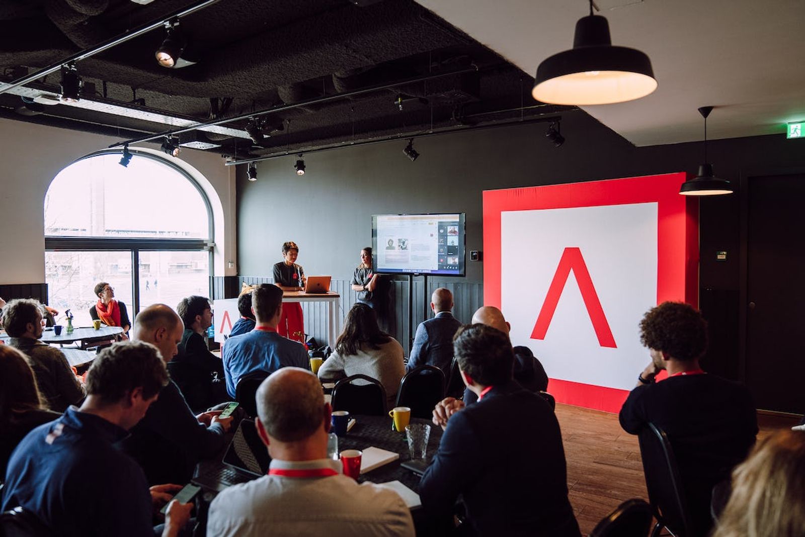 Audience sitting down watching presentation in Amsterdam with large Antler Logo sign