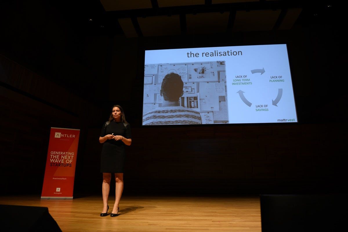 Mattrvest representative presenting on stage at Singapore Demo Day with Antler sign and presentation in the background