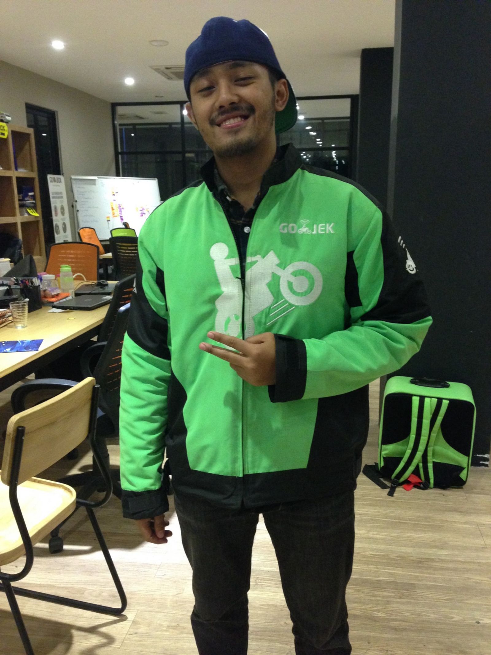 Picture of Man smiling wearing Gojek uniform with tables and chairs in background 