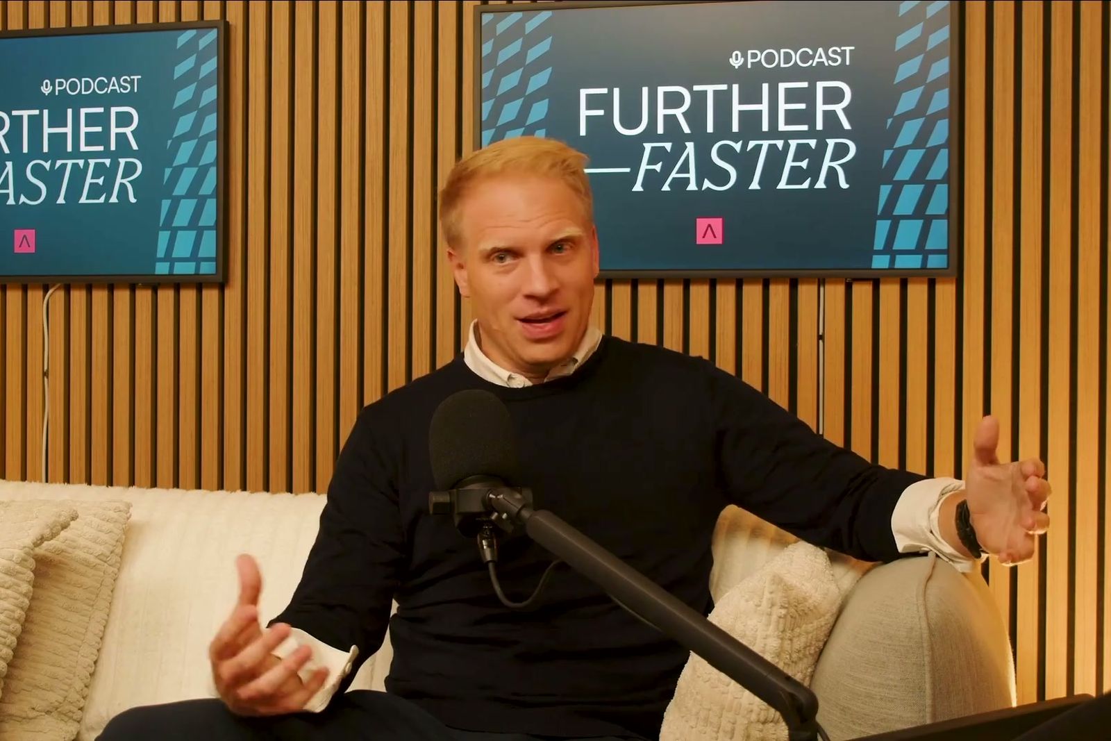 Magnus Grimeland talking with both hands on a sofa under the Further, Faster sign