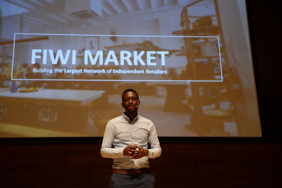 Fiwi Market representative presenting on stage at Singapore Demo Day with Fiwi Market presentation in the background