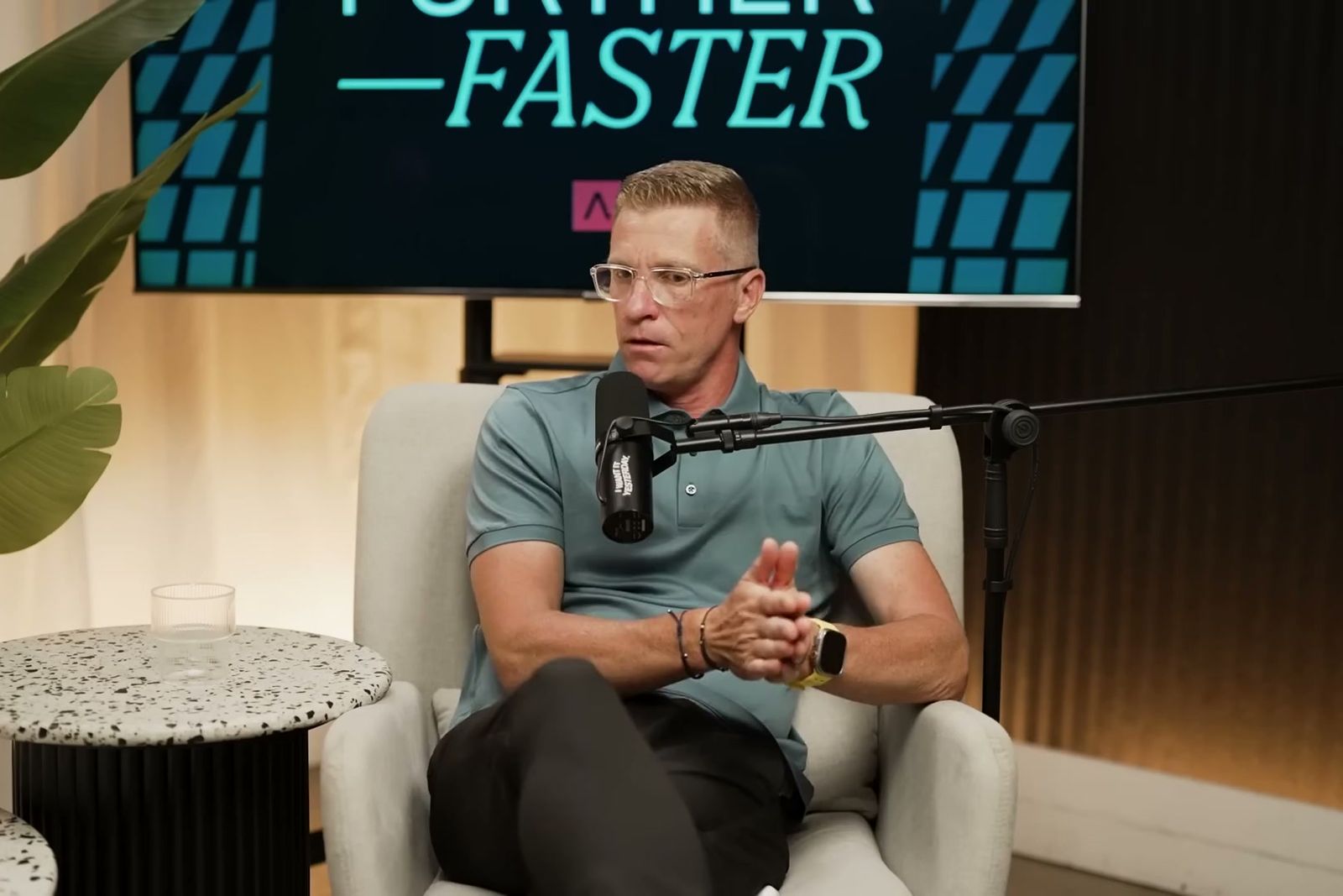 David Spindler talking at a microphone under the Further, Faster sign