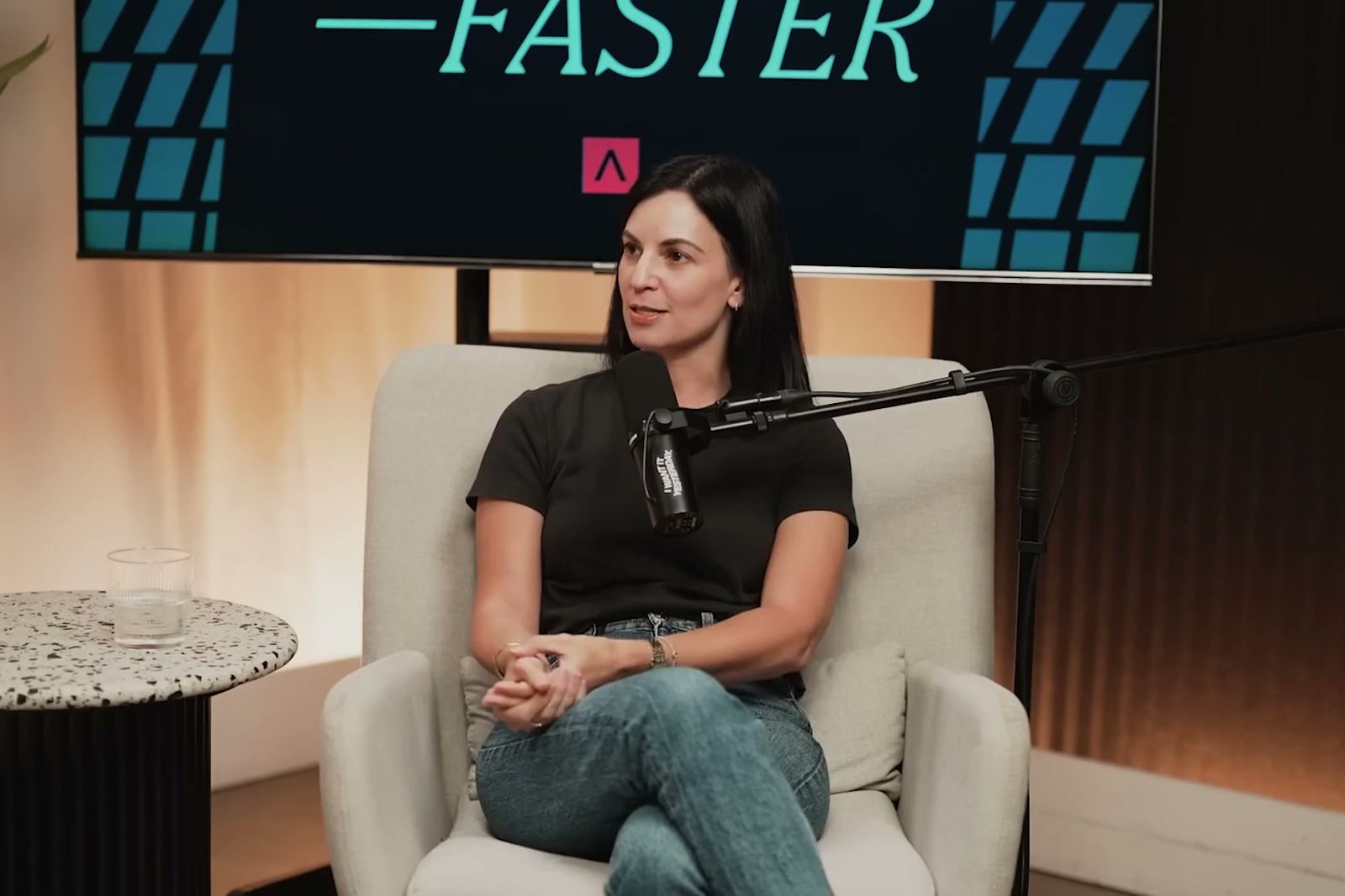 Carla Penn-Kahn in an armchair at a microphone under the Further, Faster sign