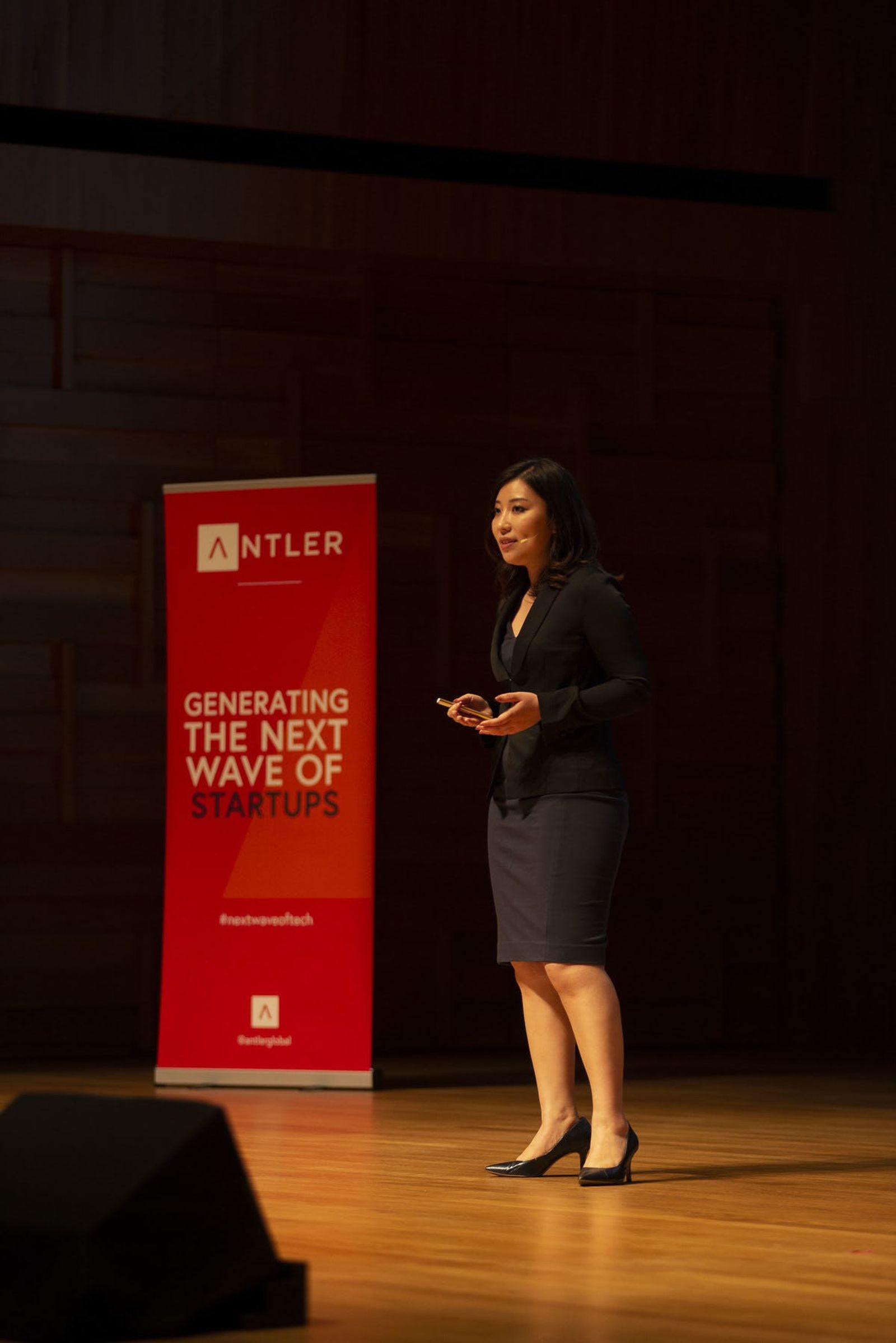 MAIC representative presenting on stage at Singapore Demo Day with Antler sign in the background 
