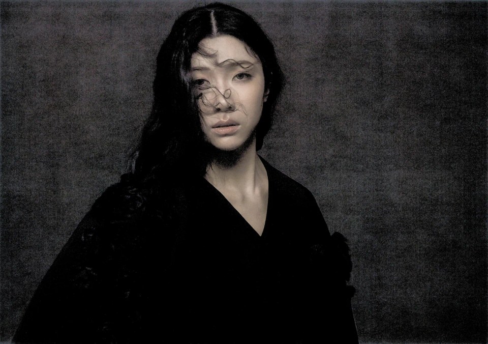 Close portrait of Sammi Chen with wind-swept hair against charcoal.