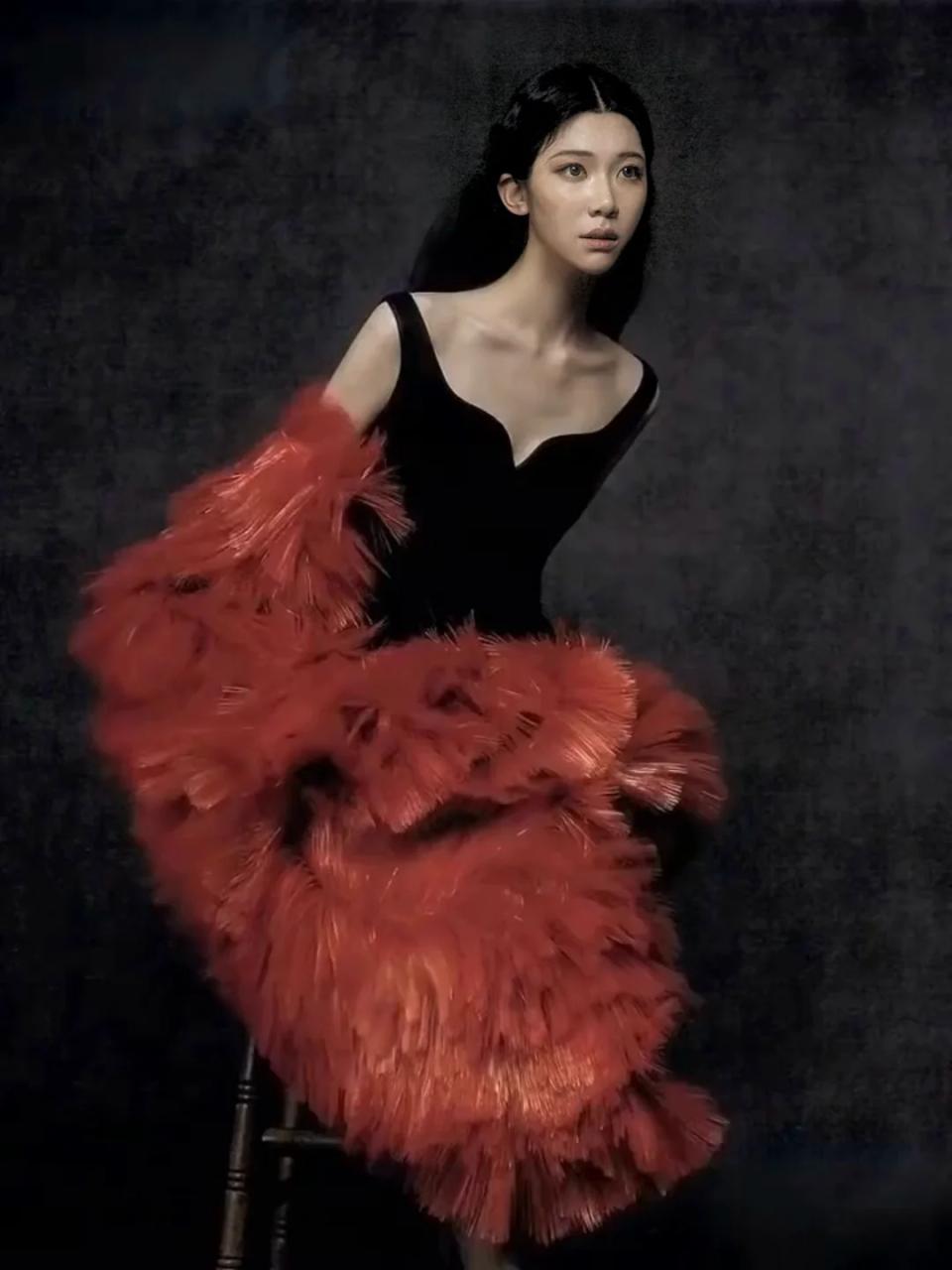 Sammi Chen seated in black with a red feather wrap against charcoal.