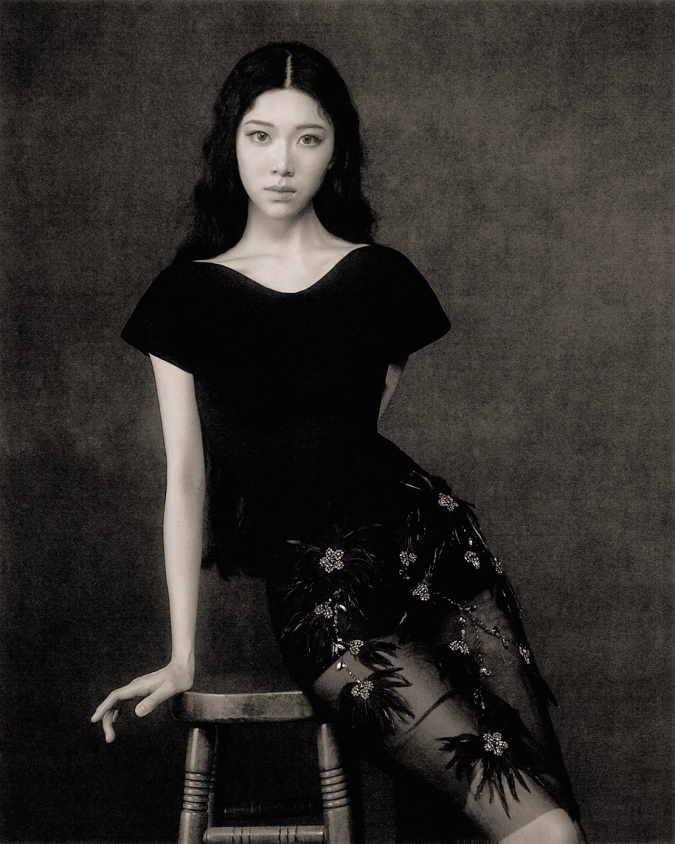Sammi Chen seated in a black dress against a charcoal backdrop.