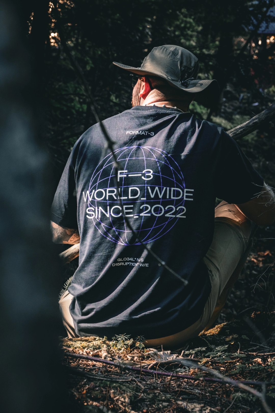 Man sitting on a natural forest wearing a black Format-3 branded t-shirt