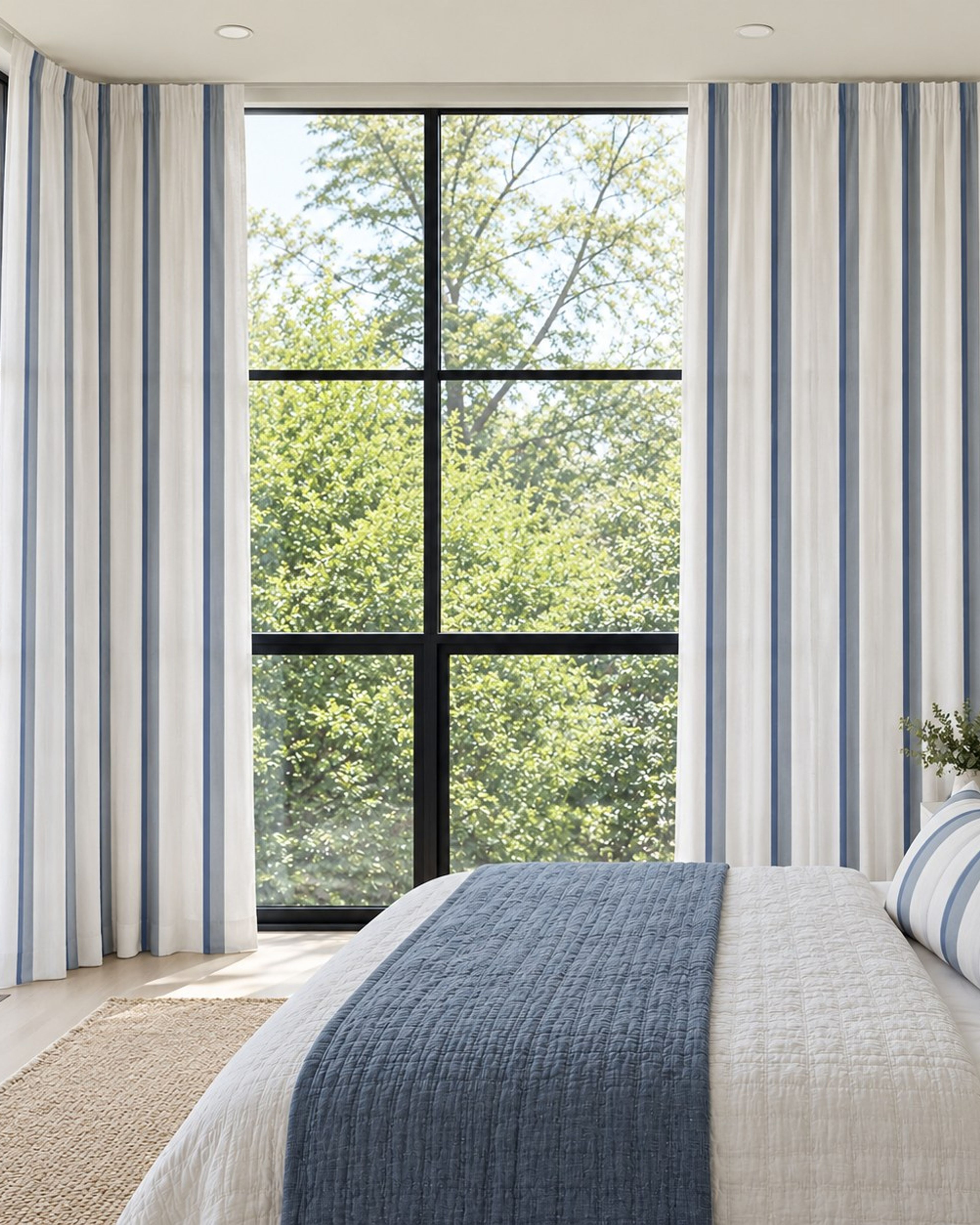 Blue striped linen textured curtains at floor to ceiling windows in a bright bedroom