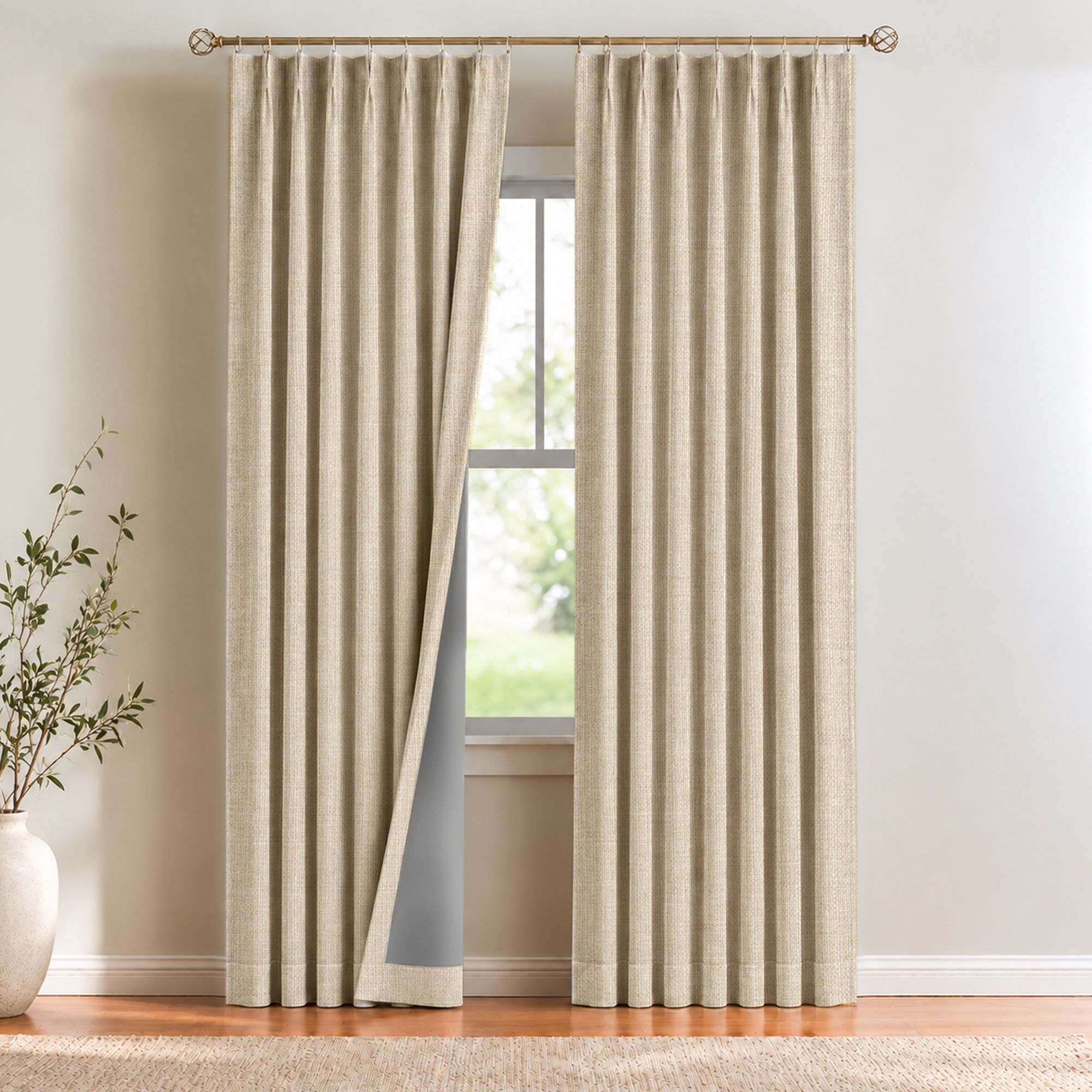 Faux linen blackout curtains in natural, pinch pleated on a brass rod beside a window