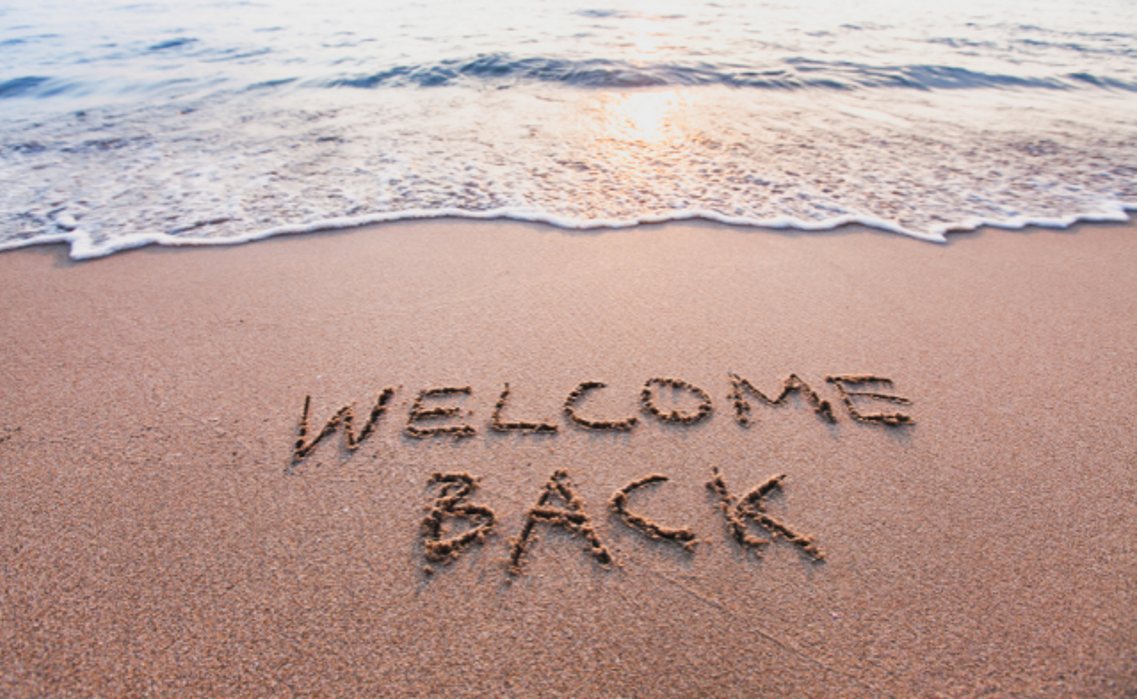"Welcome back" written in the sand at the beach