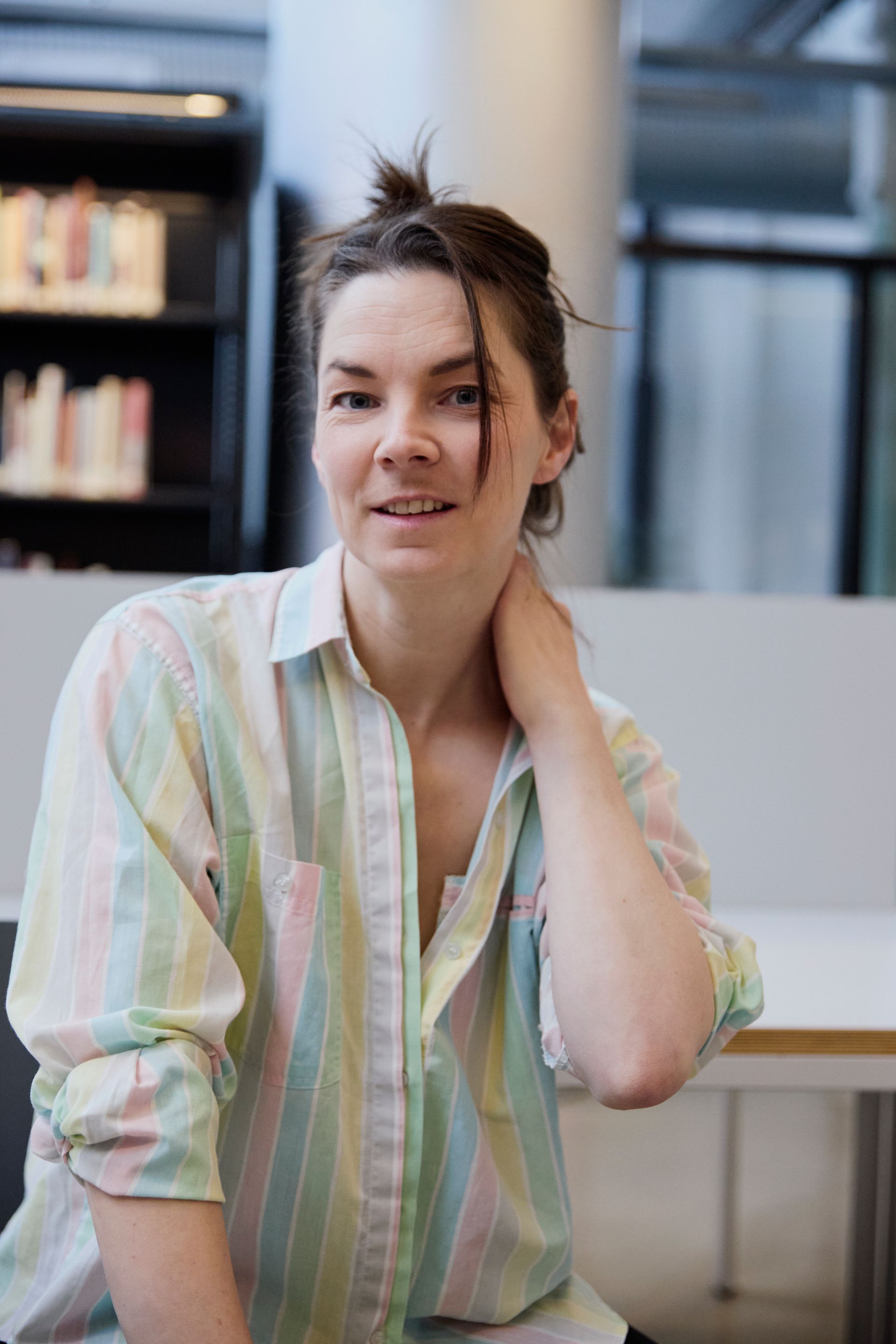 Ingrid in a pastel T-shirt smiling, her hand supporting her neck and looking straight in the camera.