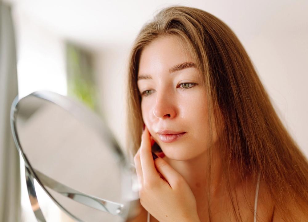 woman looking at her skin in a mirror