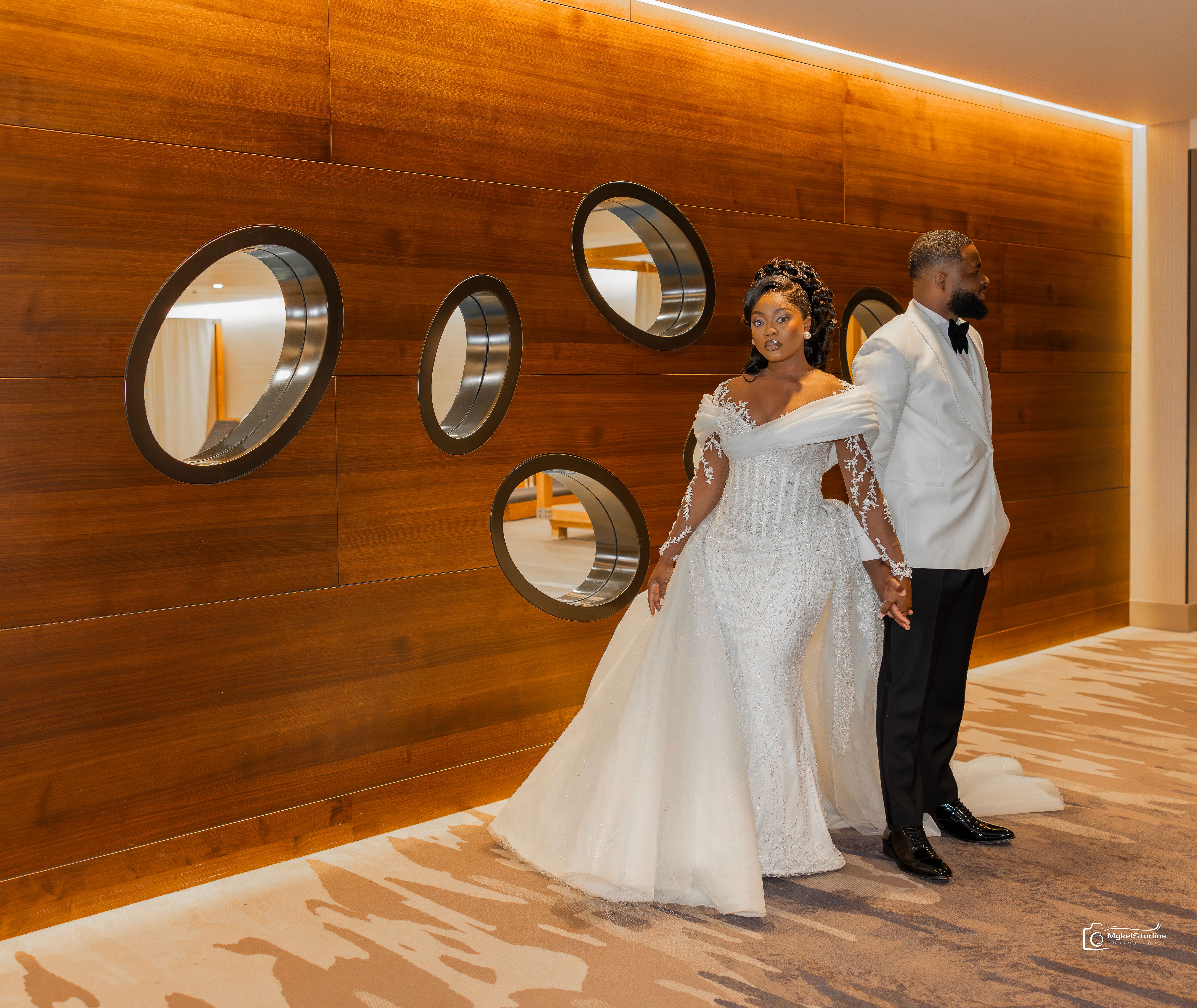 Bride and groom standing in front of a bright wall