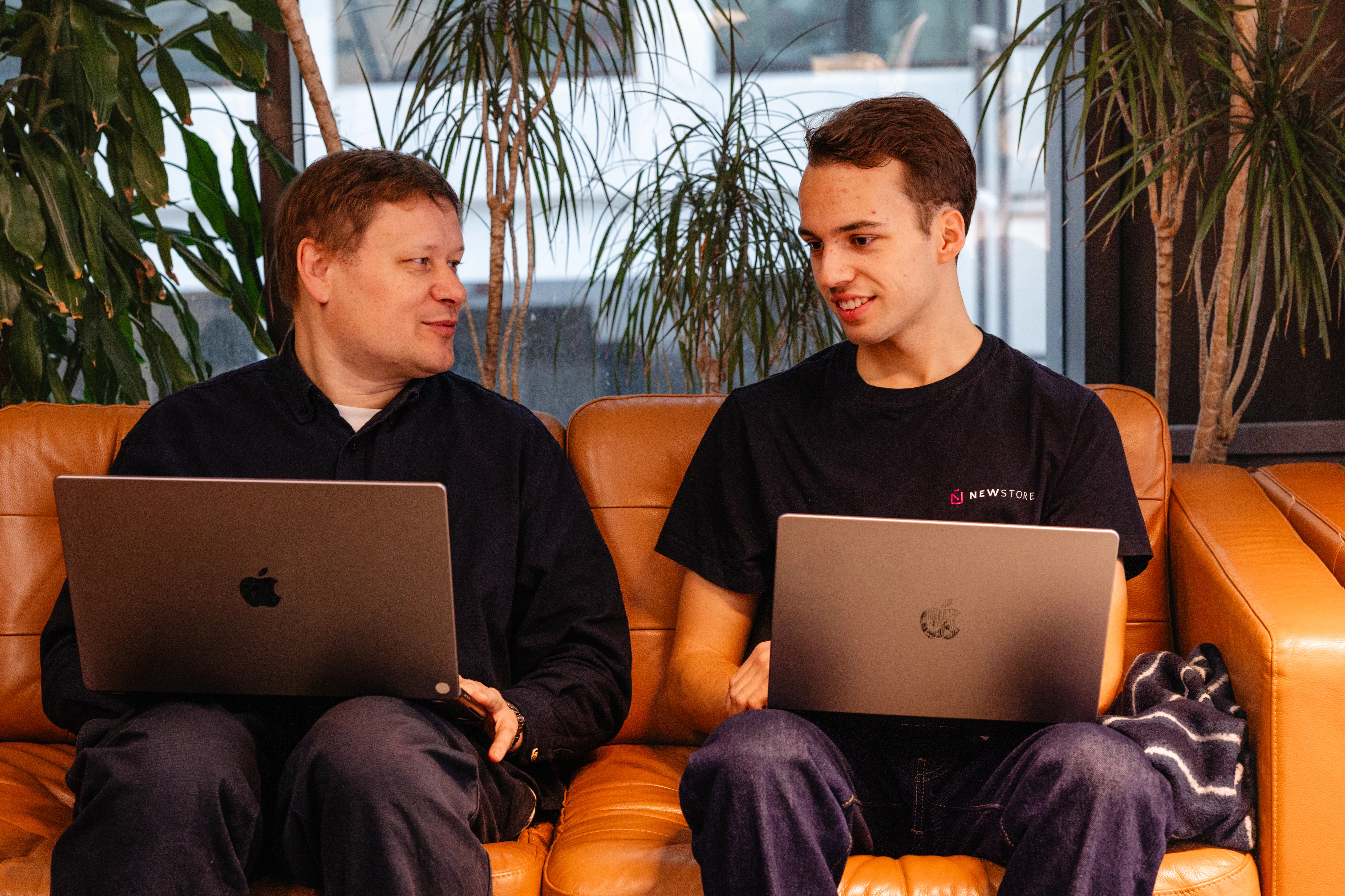 two men are sitting on a couch with laptops .