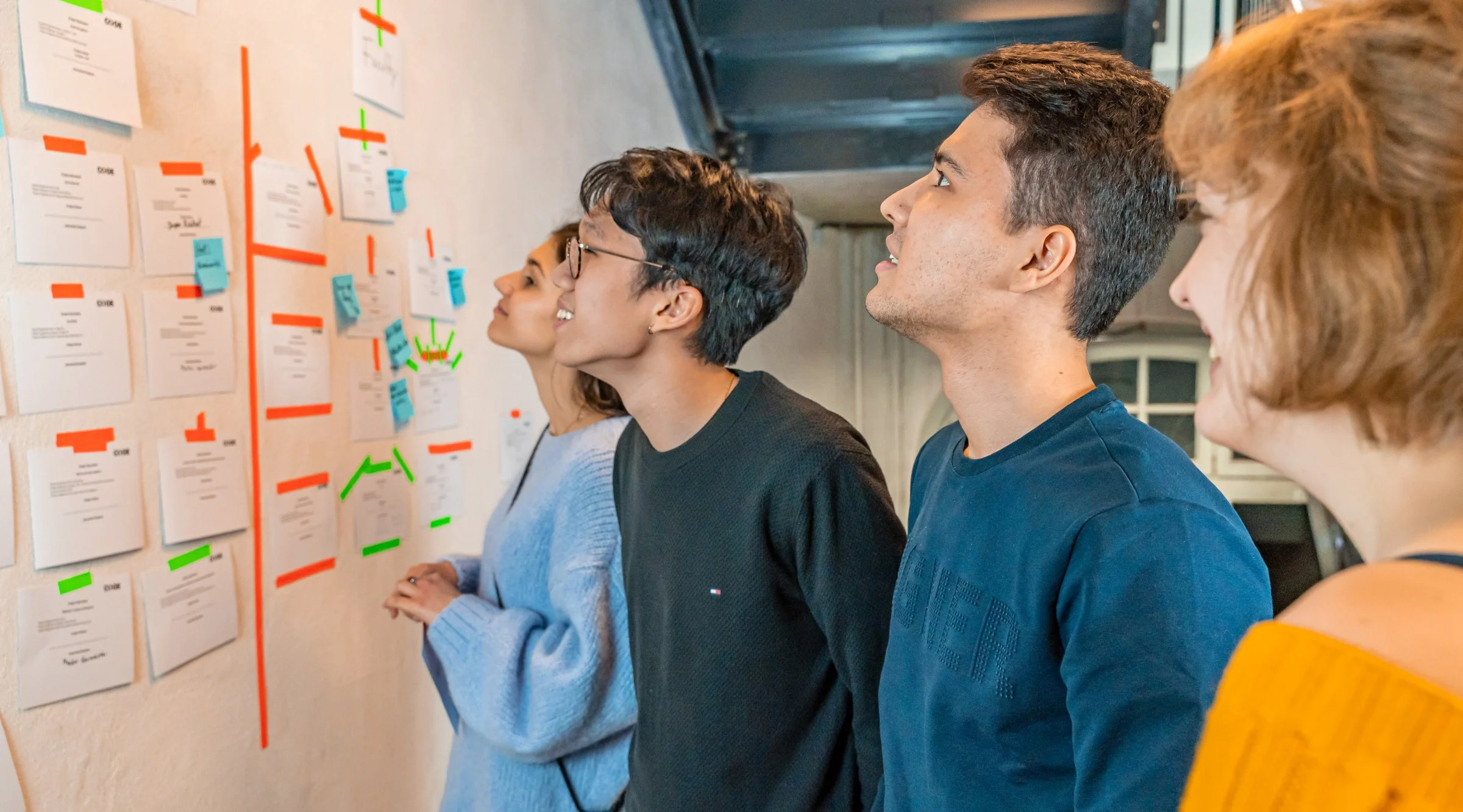 a group of young people are looking at a whiteboard with sticky notes on it .
