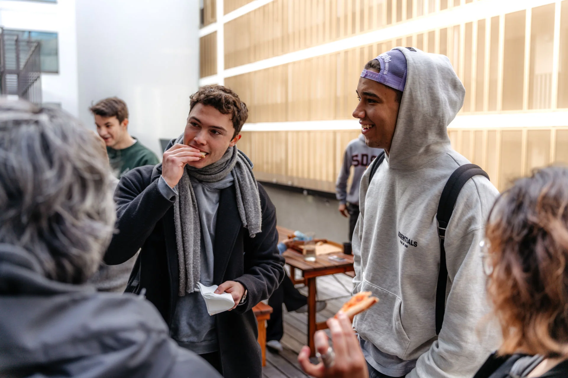 a group of young men are standing around a table eating pizza .