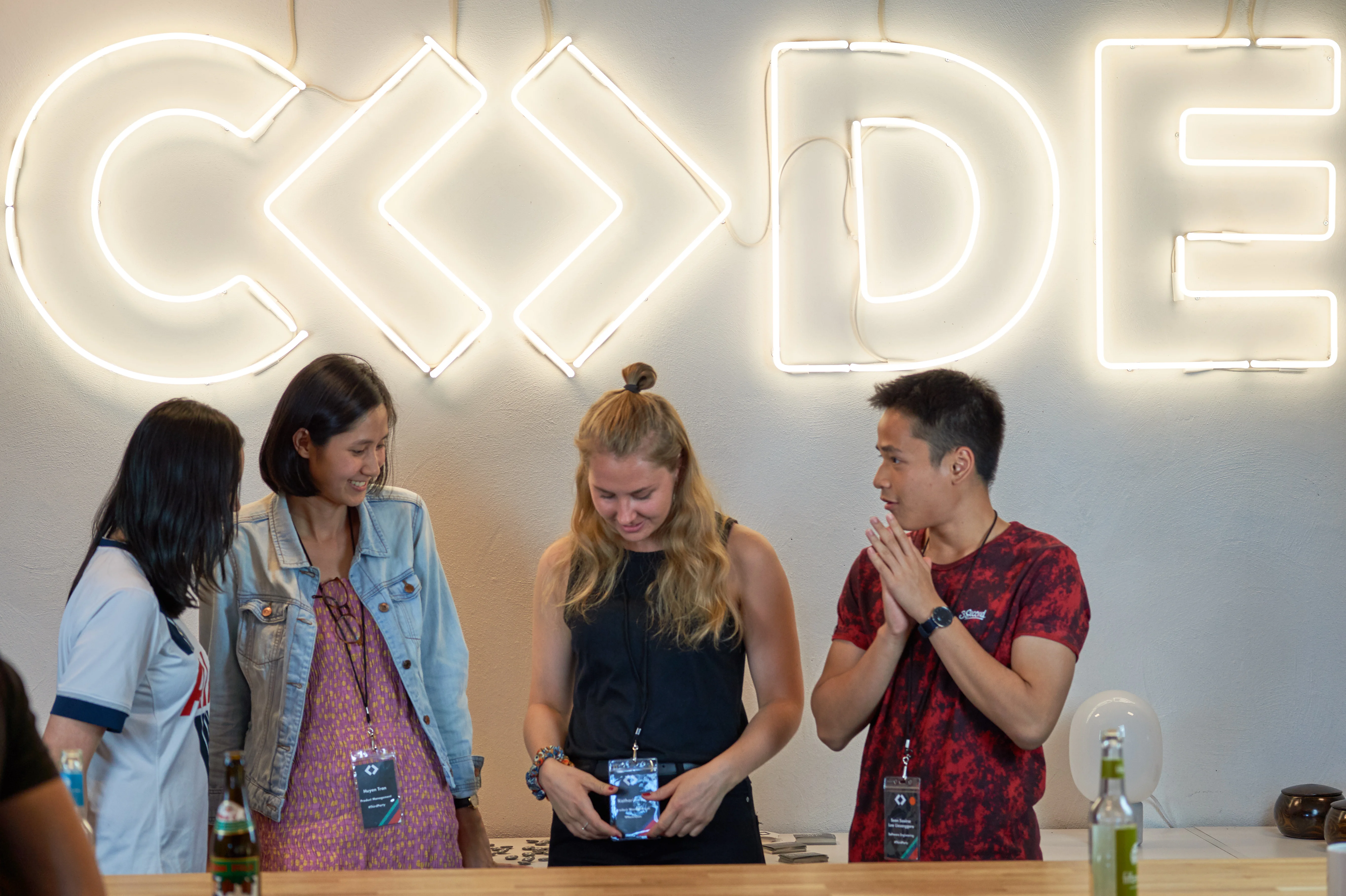 a group of people are standing around a table in front of a neon sign that says `` code '' .