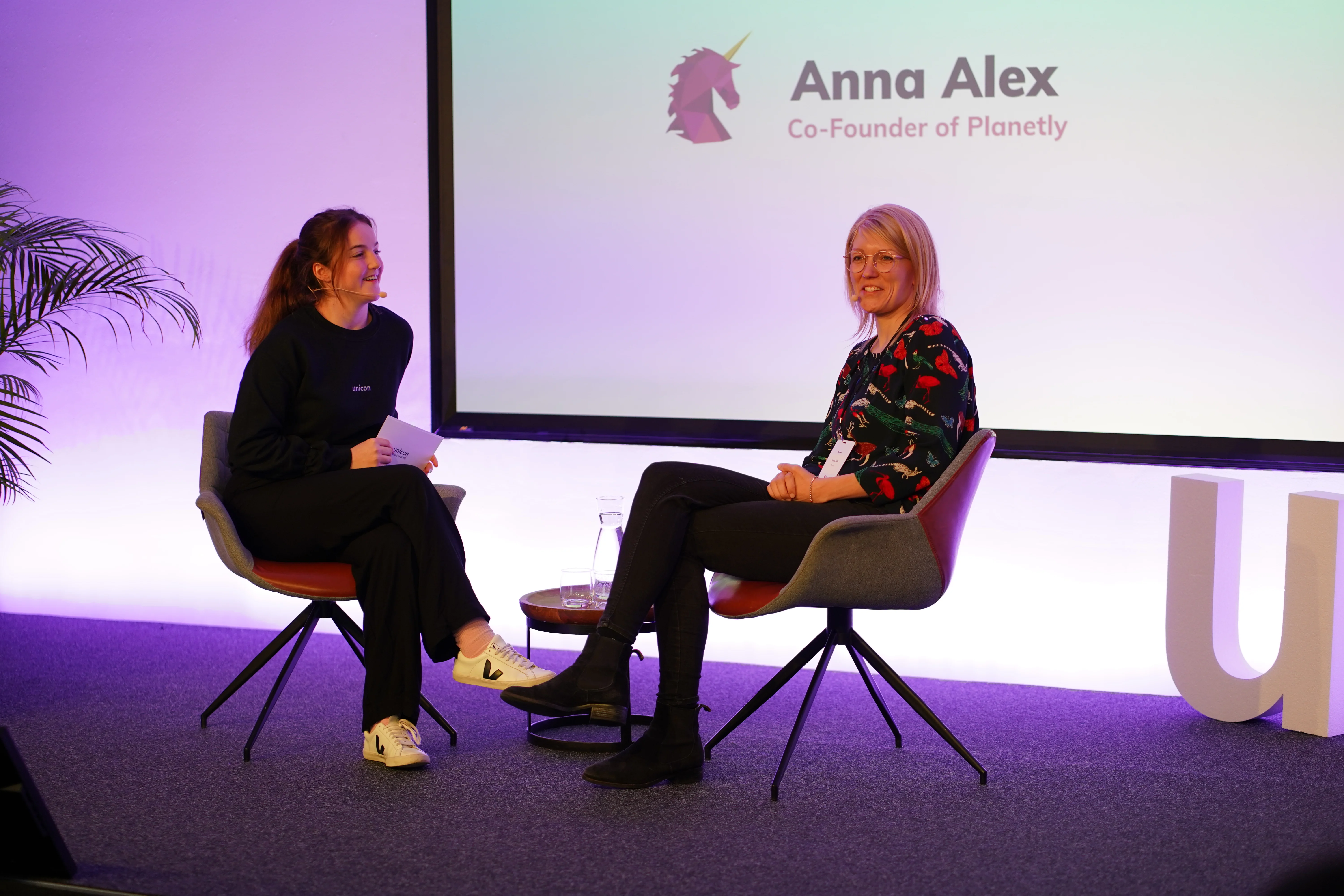 two women are sitting in chairs on a stage talking to each other .