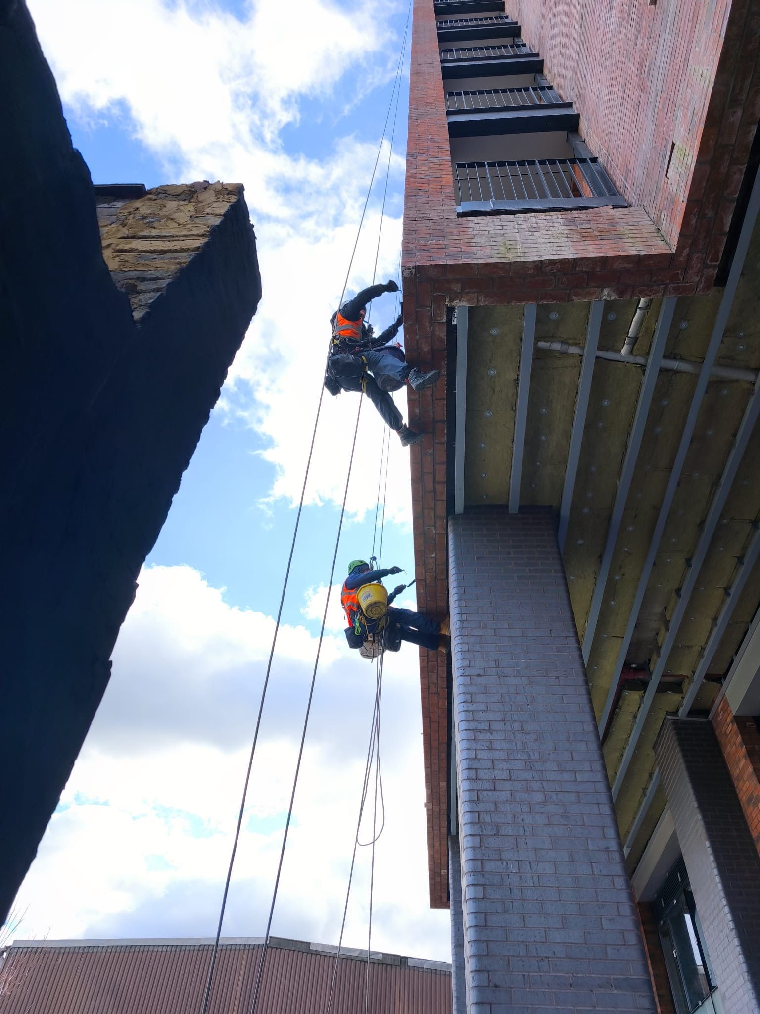 Two rope access technicians carrying out high-level brickwork repairs on a building façade.