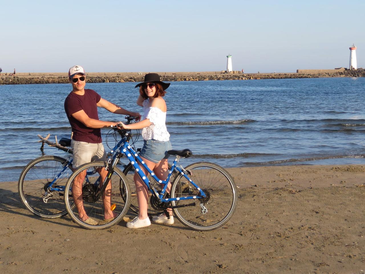 Couple avec leurs vélos sur la plage, phare au loin