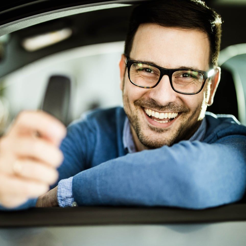 Smiling man with glasses inside car holding keys after completing purchase through Drivvn automotive eCommerce platform