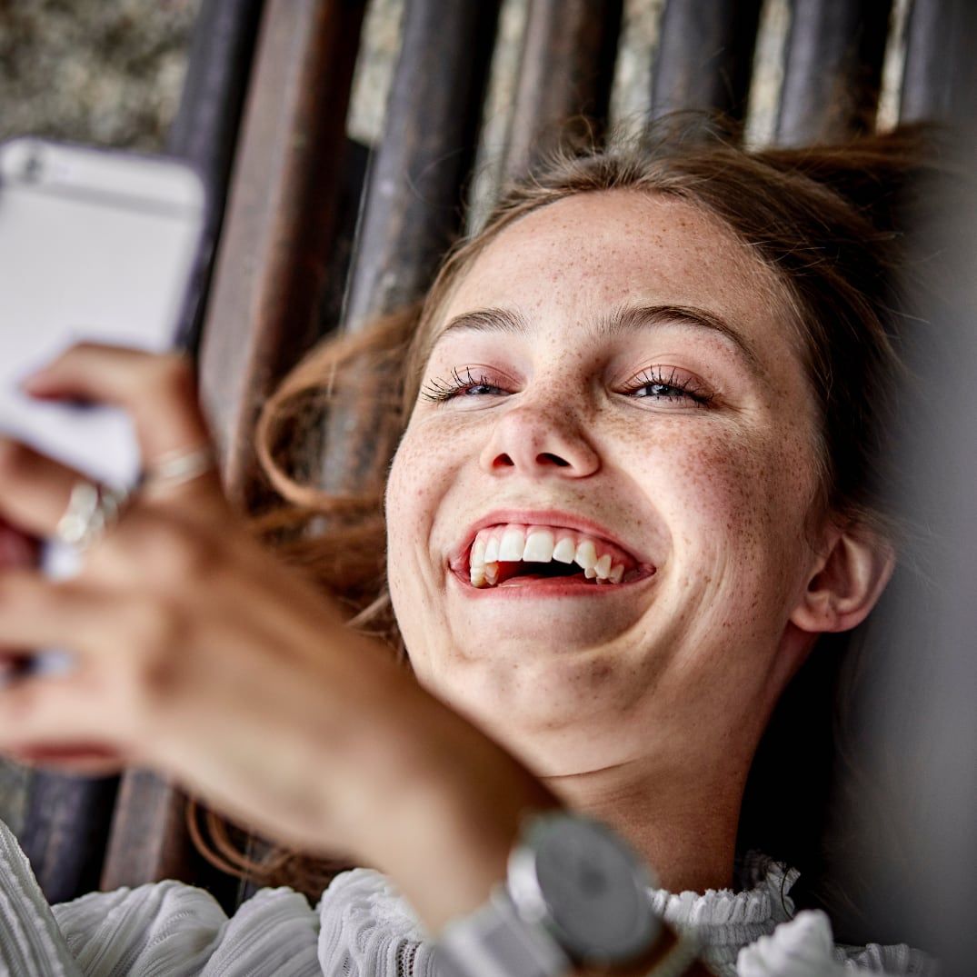 Happy woman laughing while shopping for vehicles on Drivvn eCommerce platform using smartphone