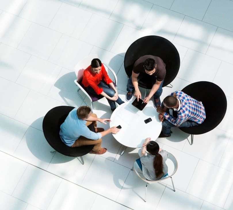 Five people sat on chairs at a low round table talking in a light and modern workspace