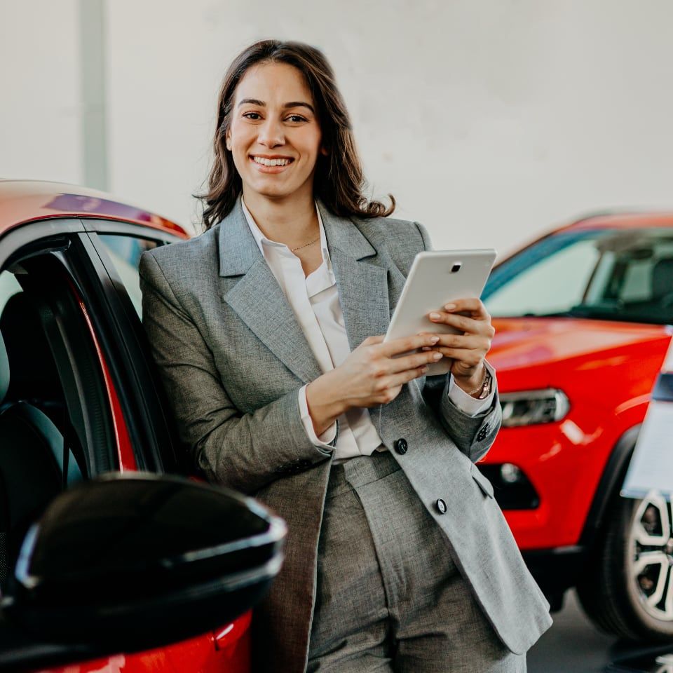 Professional woman in gray blazer using tablet to manage Drivvn automotive eCommerce platform in car dealership showroom