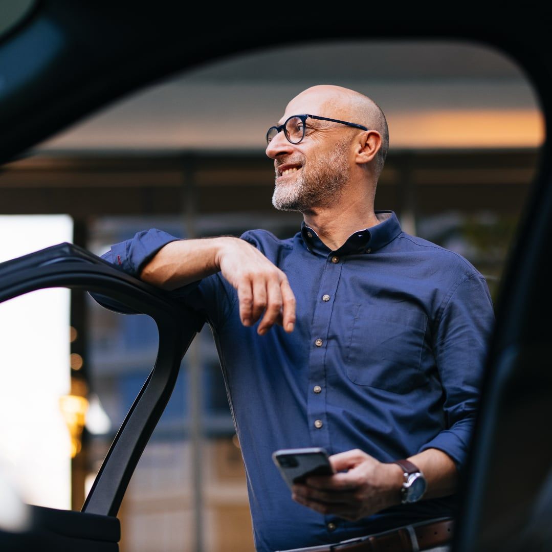 Satisfied middle-aged man with glasses and beard standing by car after completing purchase through Drivvn automotive eCommerce platform