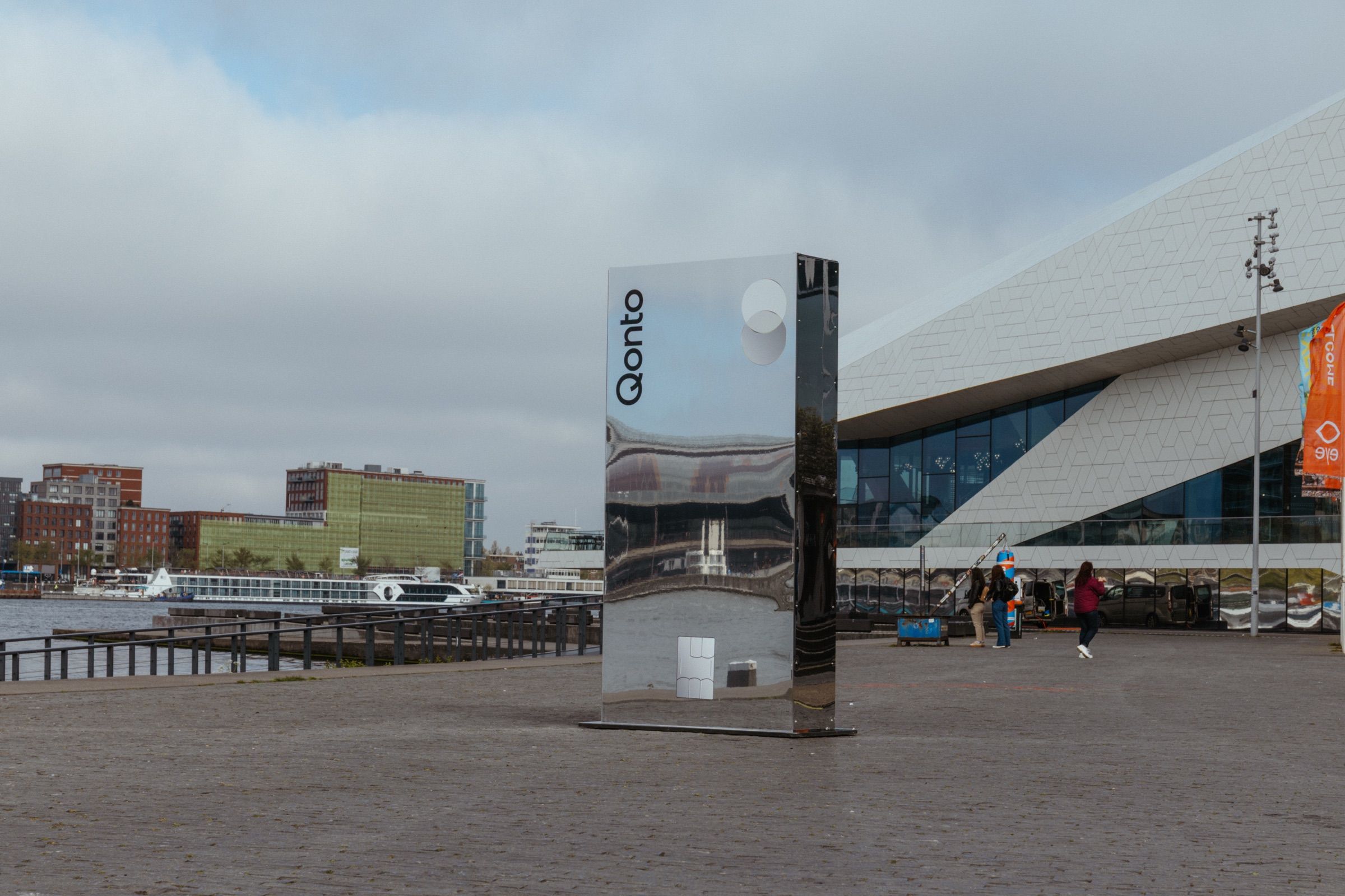 A tall mirror pillar with the Qonto mark in front of the EYE film museum, Amsterdam