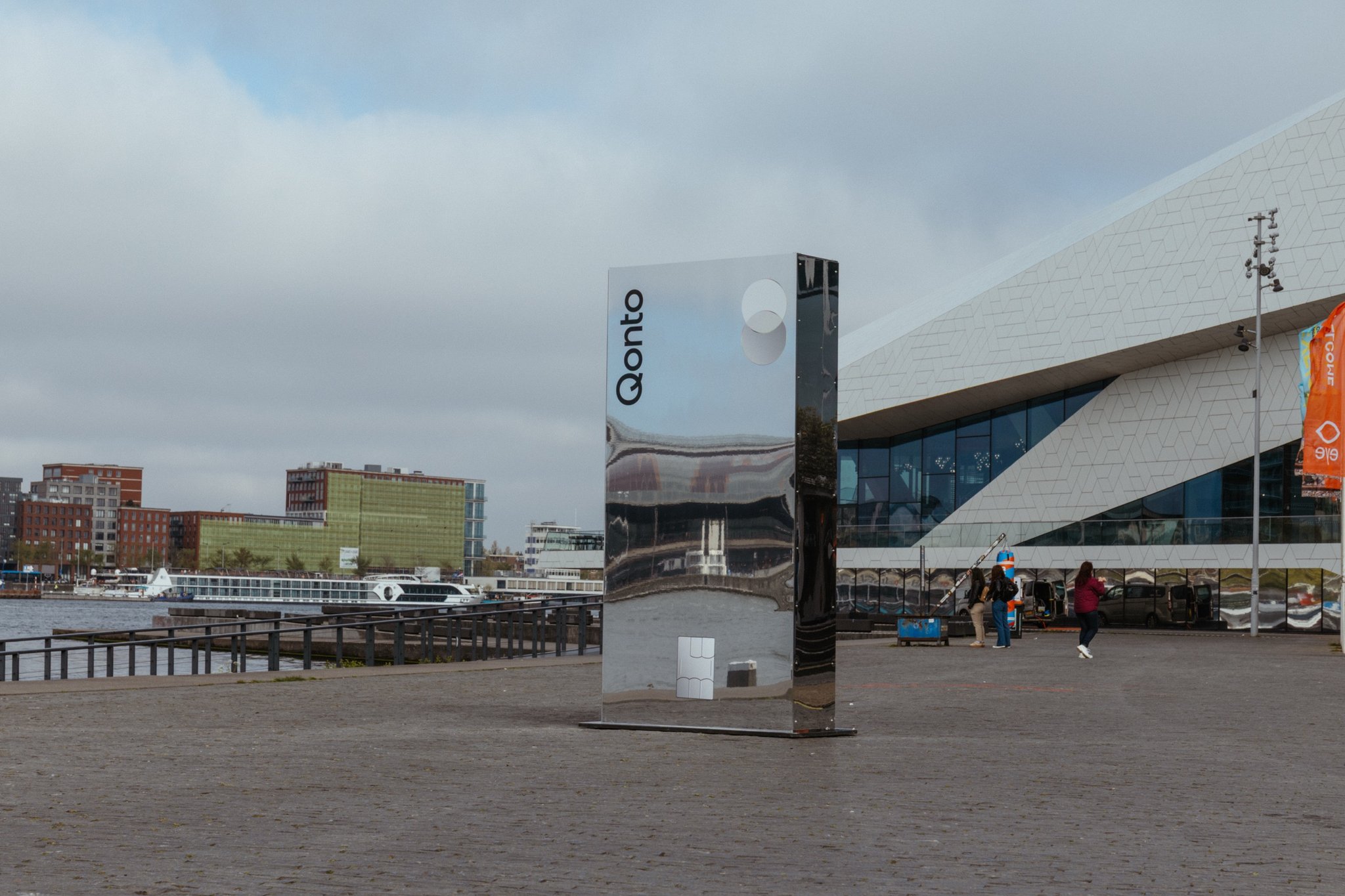 A tall mirror pillar with the Qonto mark in front of the EYE film museum, Amsterdam