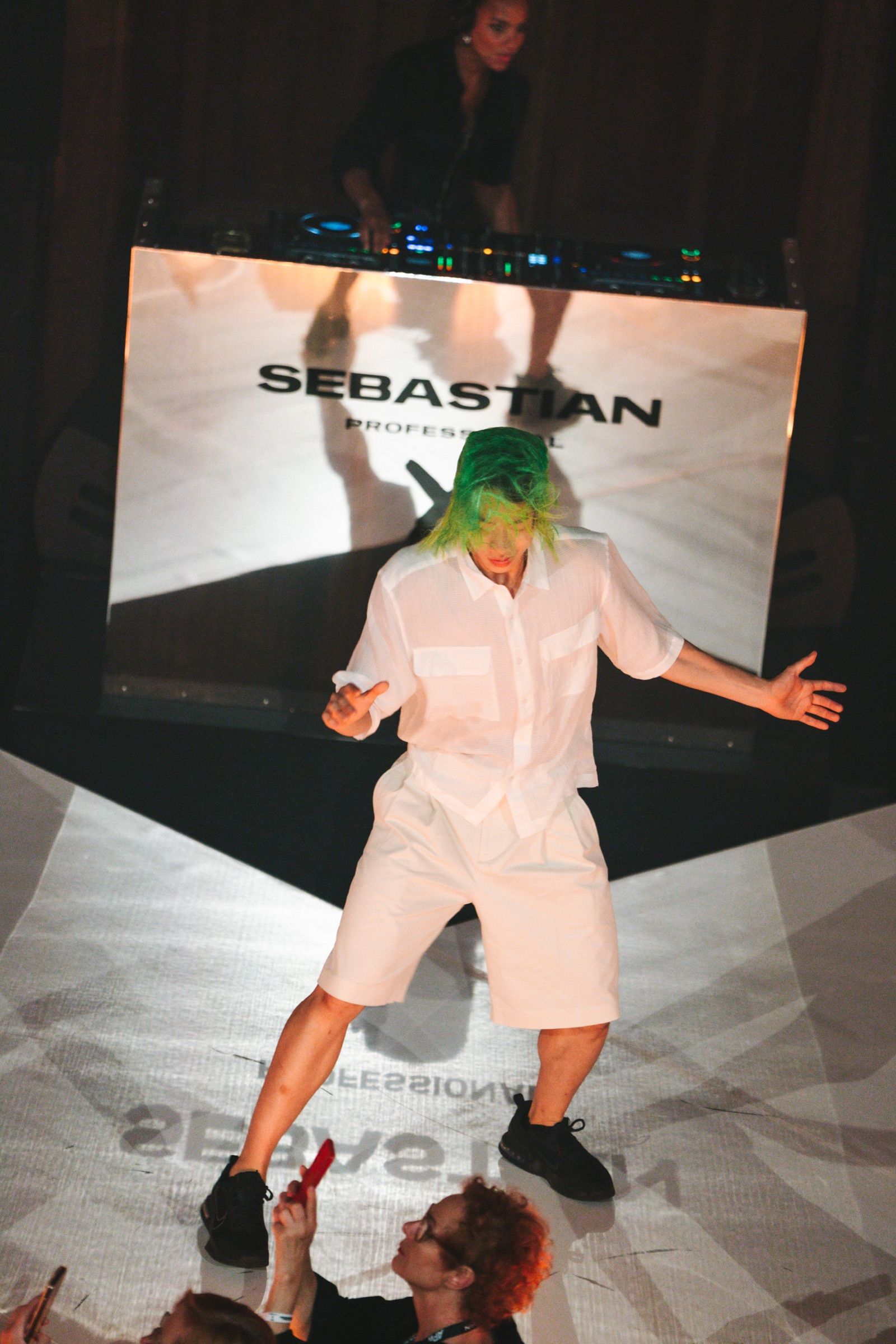 A performer on the runway in front of the mirror DJ booth with the Sebastian Professional mark
