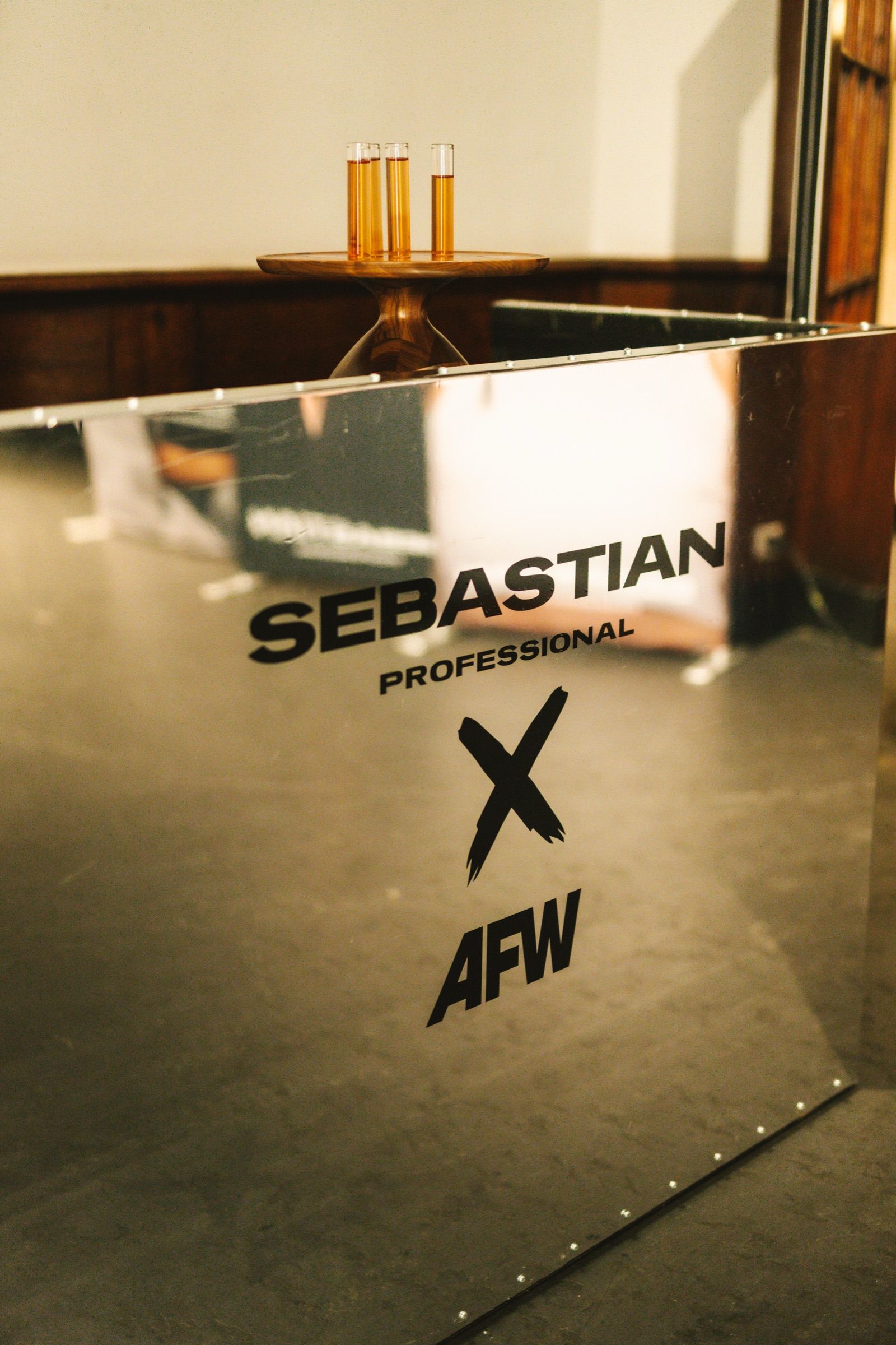 Mirror bar with the Sebastian Professional × AFW mark, glasses on a small table behind