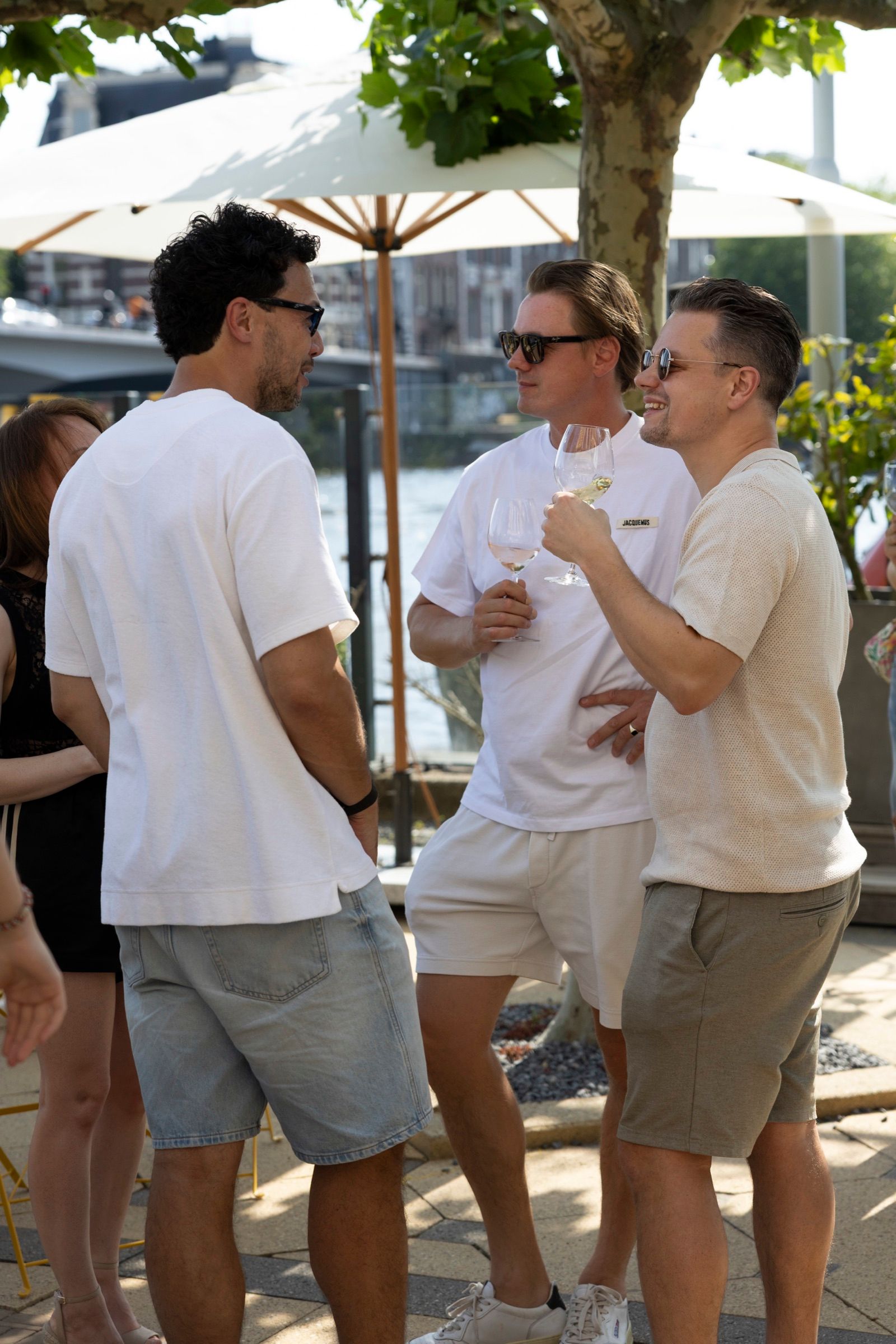 Three guests with wine glasses under a parasol by the water