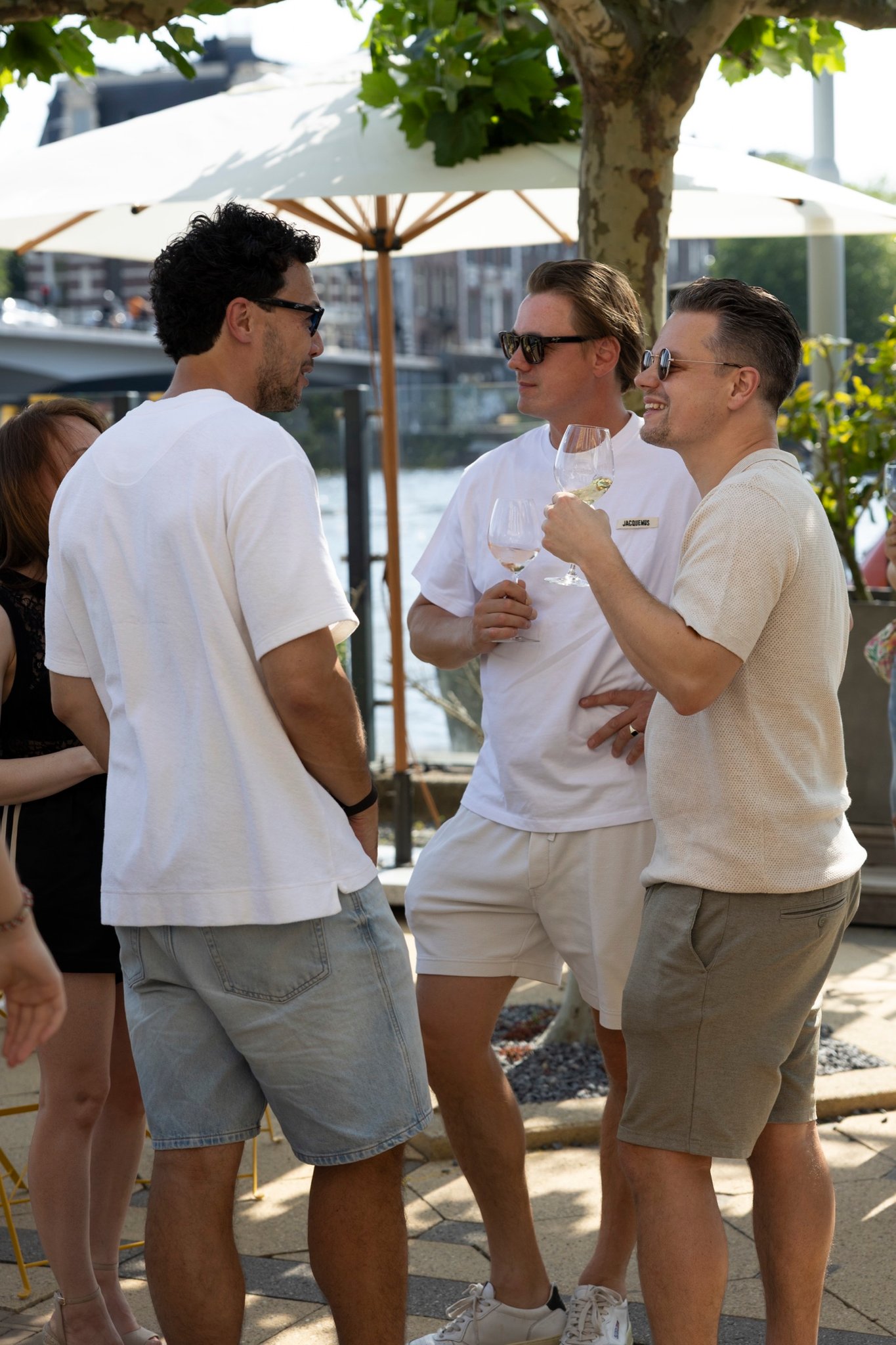 Three guests with wine glasses under a parasol by the water