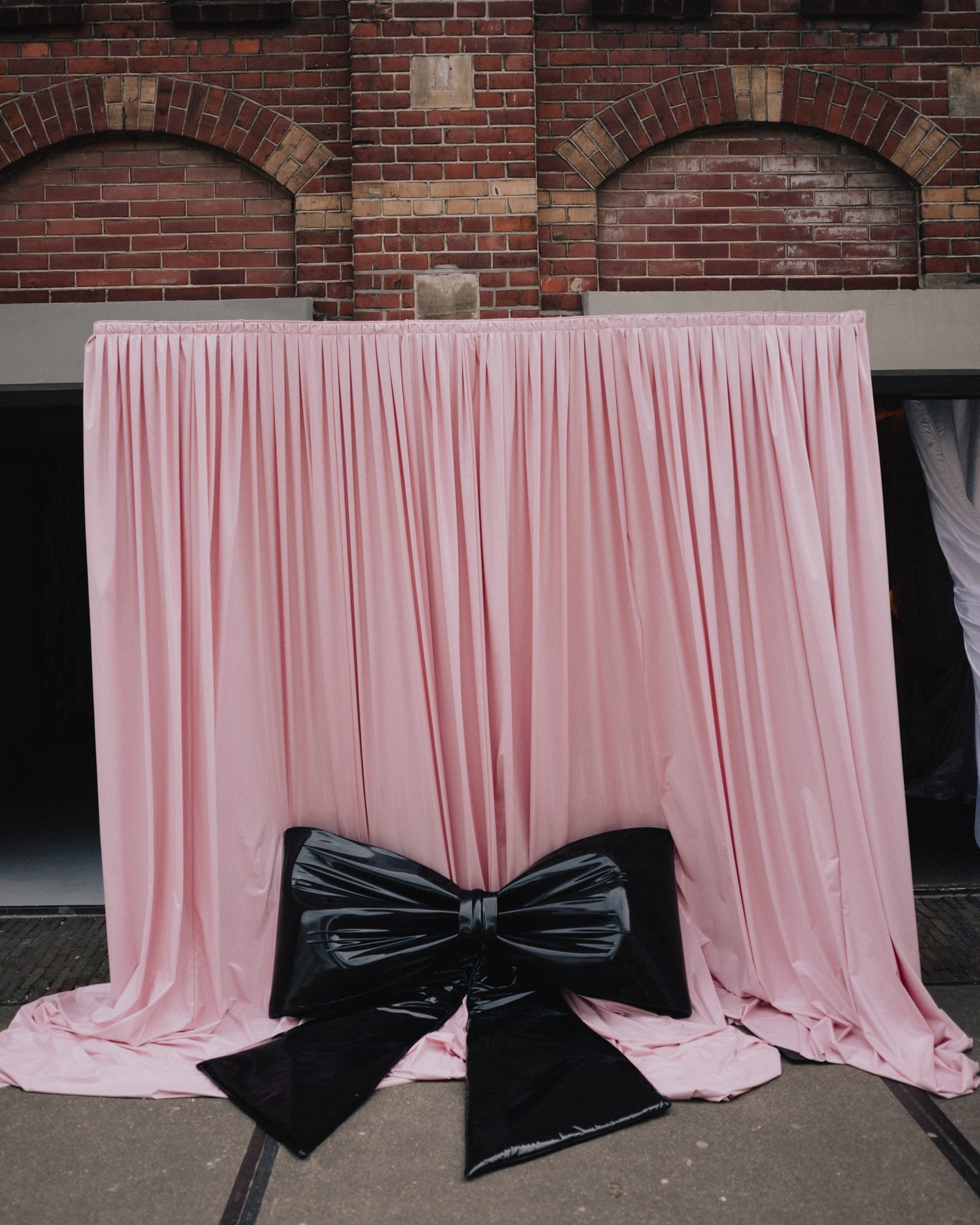 Pink laque drape with a black latex bow against a brick facade