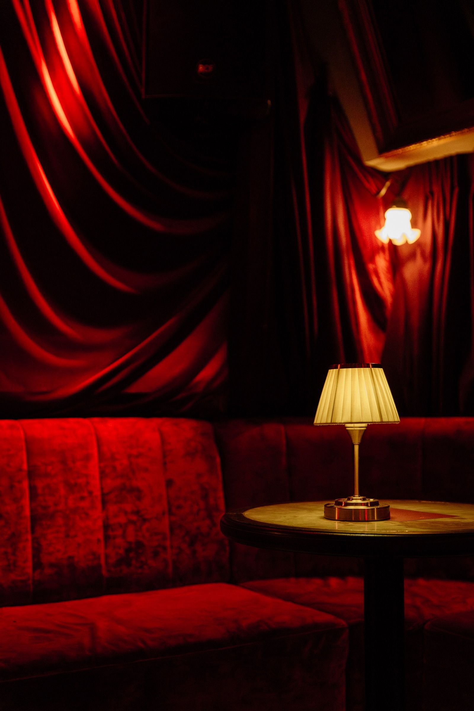 Red velvet drapes and a red velvet sofa with a small lamp on a round table