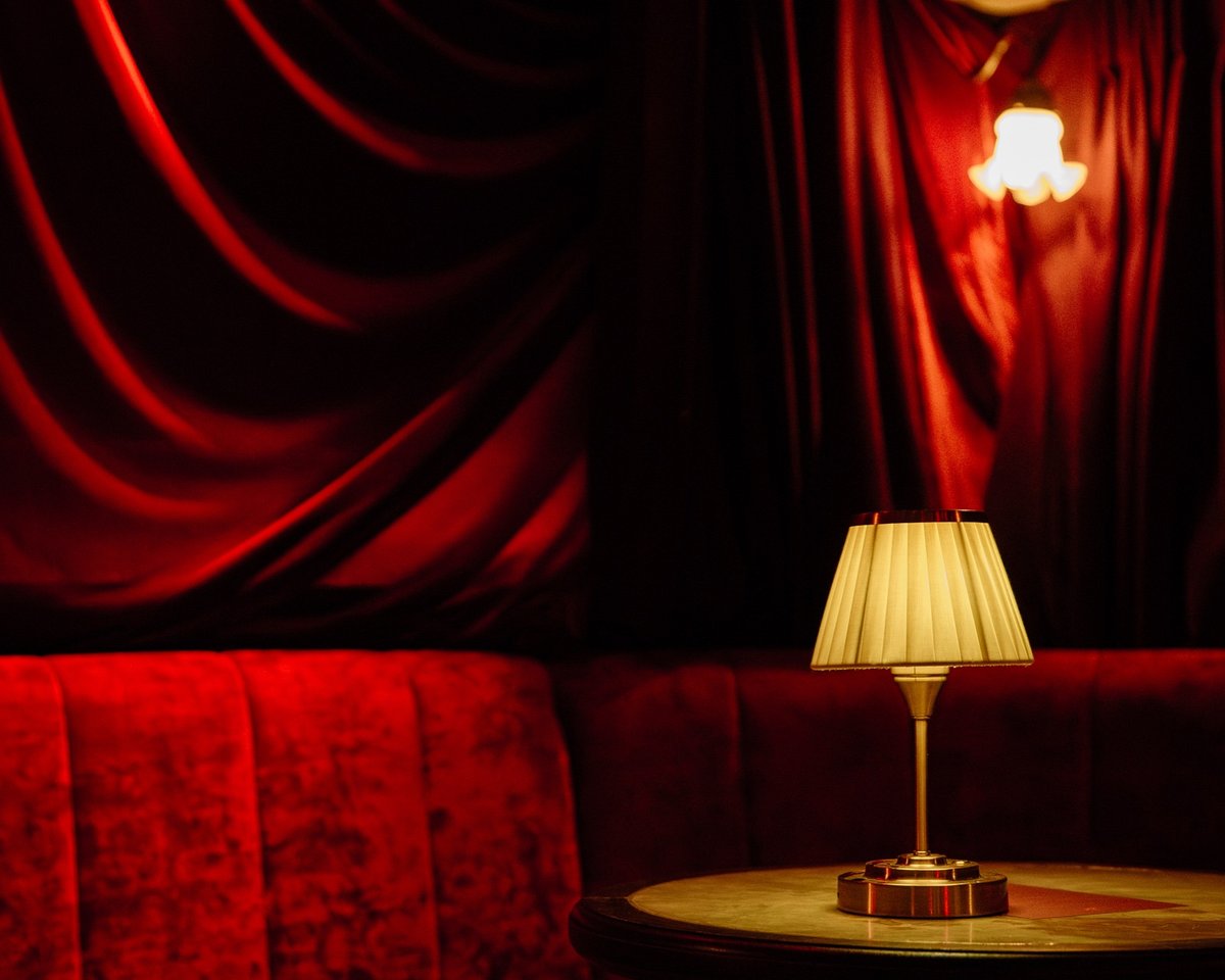 Red velvet drapes and a red velvet sofa with a small lamp on a round table