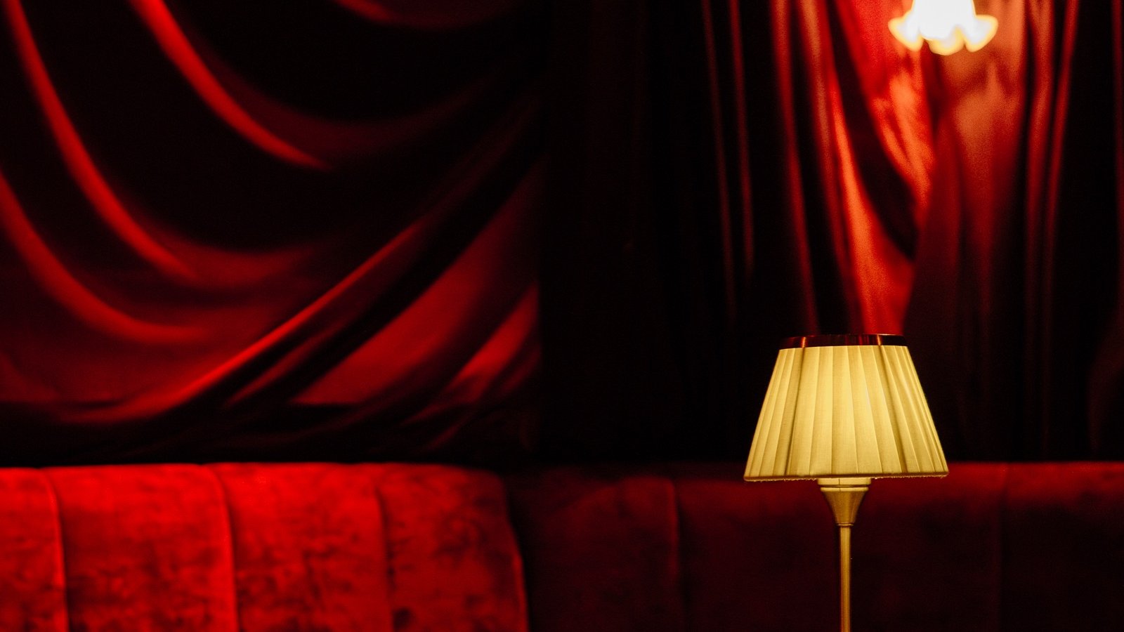 Red velvet drapes and a red velvet sofa with a small lamp on a round table