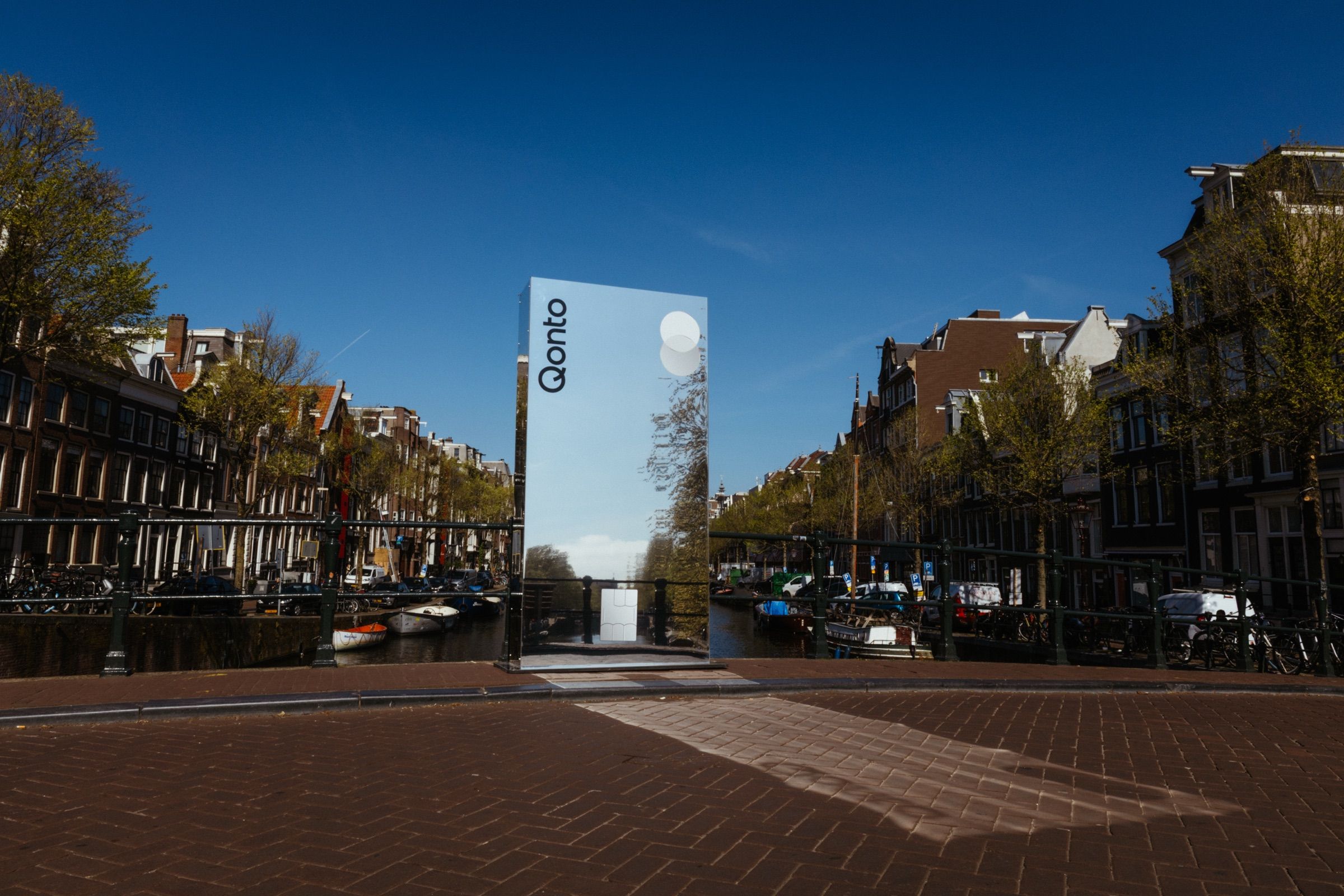 A mirror pillar on a canal bridge reflecting the Amsterdam canal houses and sky